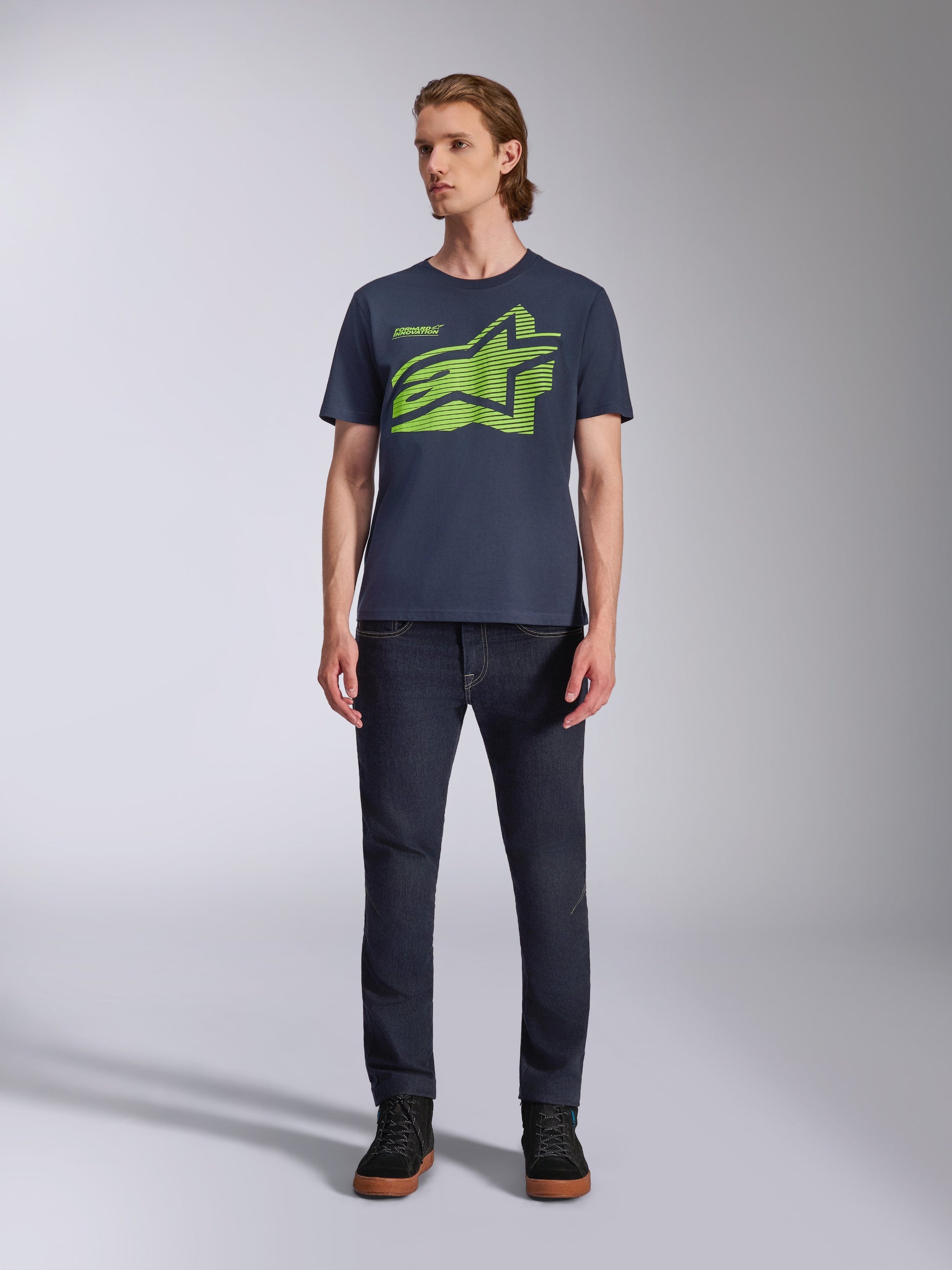 Alpinestars Fasting CSF Tee, T-shirt met korte mouwen, navy blauw met limegroen geometrisch Astars-logo, casual motorsport streetwear, man draagt het T-shirt met een donkere spijkerbroek