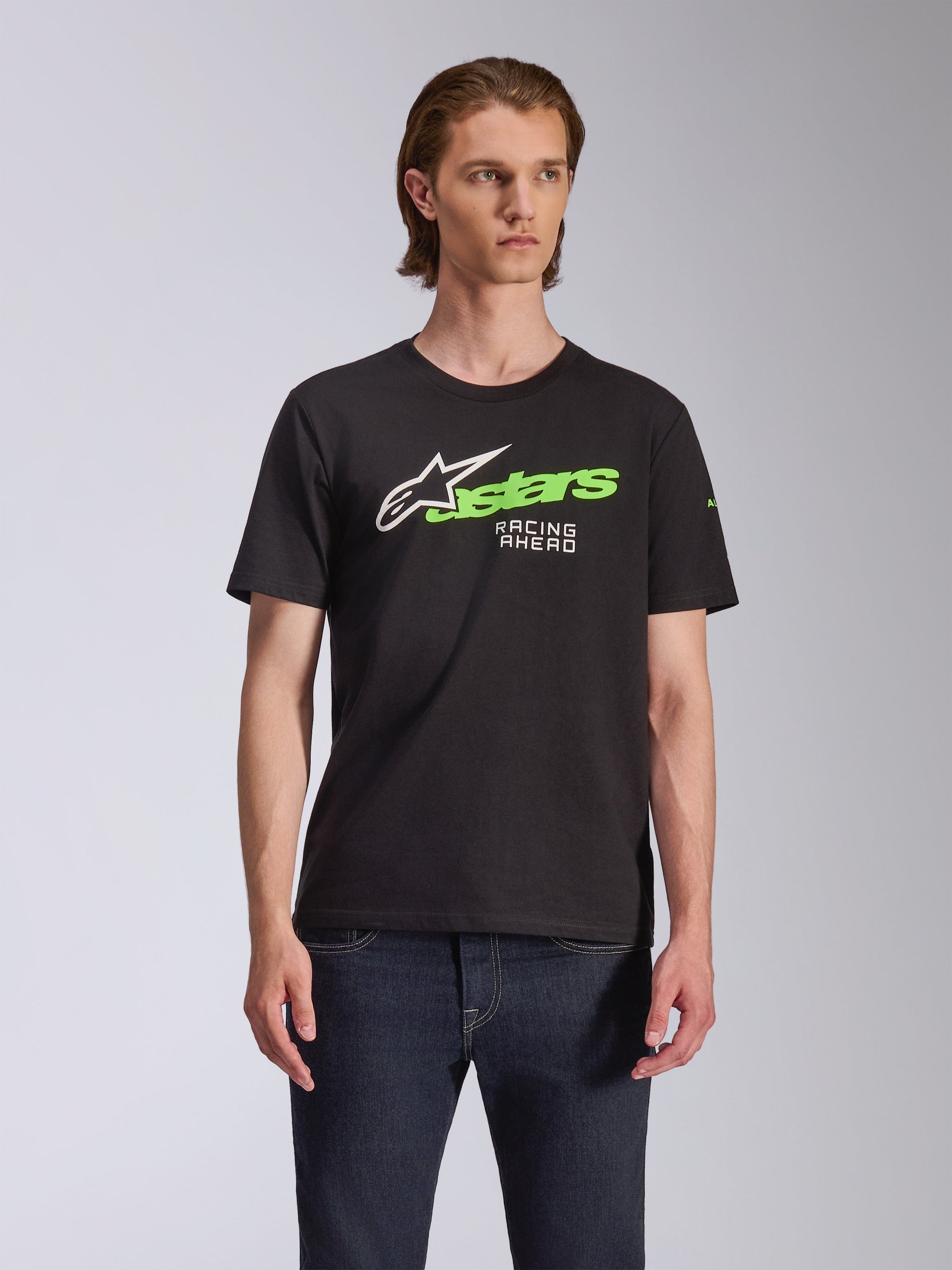 Alpinestars Entitled CSF Tee, t-shirt met korte mouwen, zwart, met een wit en limoengroen Alpinestars-logo met 'Racing Ahead' tekst, casual motorsport-geïnspireerd ontwerp, model draagt shirt met donkere jeans