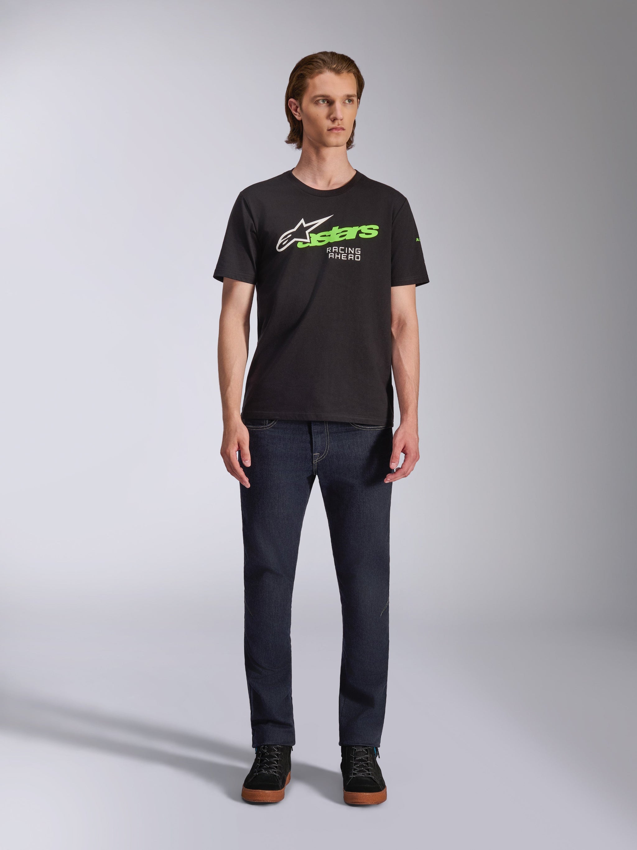 Alpinestars Entitled CSF Tee, T-shirt met korte mouwen, zwart, voorzien van een wit sterlogo, neon groene 'stars' tekst en 'Racing Ahead' graphic op de borst, gedragen door een model met een donkere jeans, casual motorsport-geïnspireerde kleding