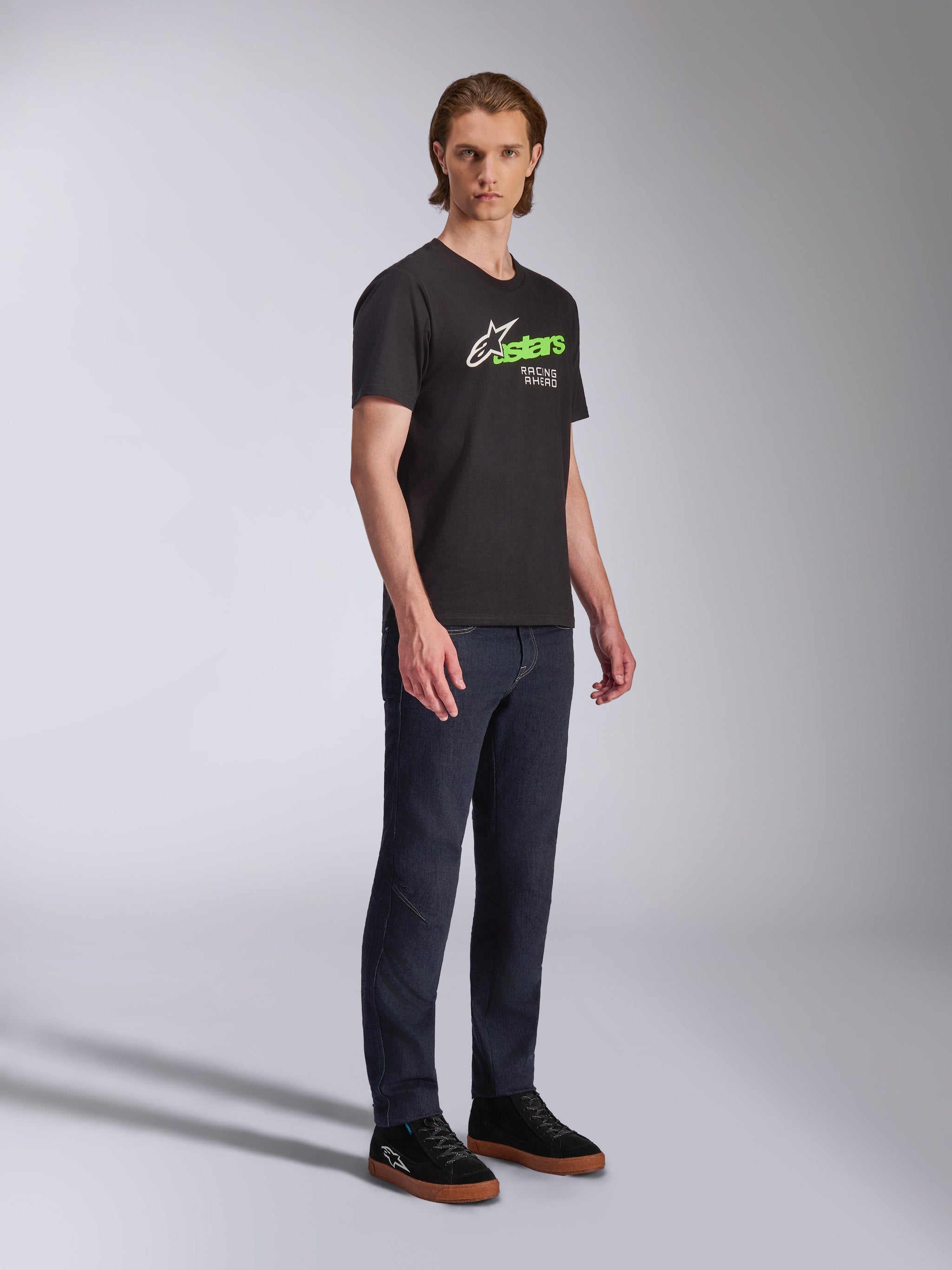 Alpinestars Entitled CSF Tee, T-shirt met korte mouwen, zwart, witte en groene graphic met 'Racing Ahead' tekst, gedragen met donkere jeans en zwarte sneakers, casual motorsport streetwear