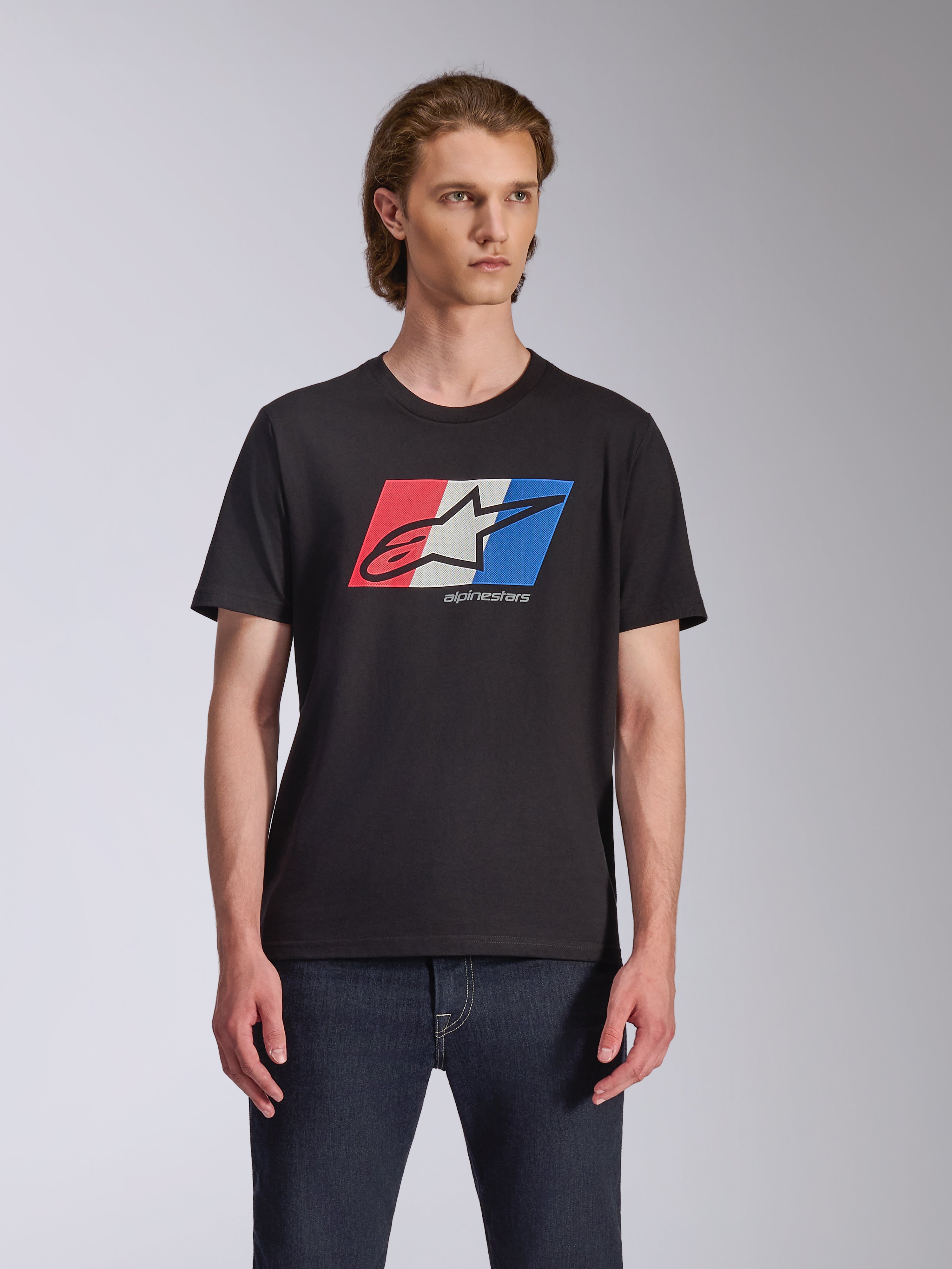 Alpinestars Global CSF Tee, T-shirt met korte mouwen, zwart, rood wit en blauw Ageless logo graphic, gedragen door mannelijk model met donkere jeans, casual motorsport streetwear
