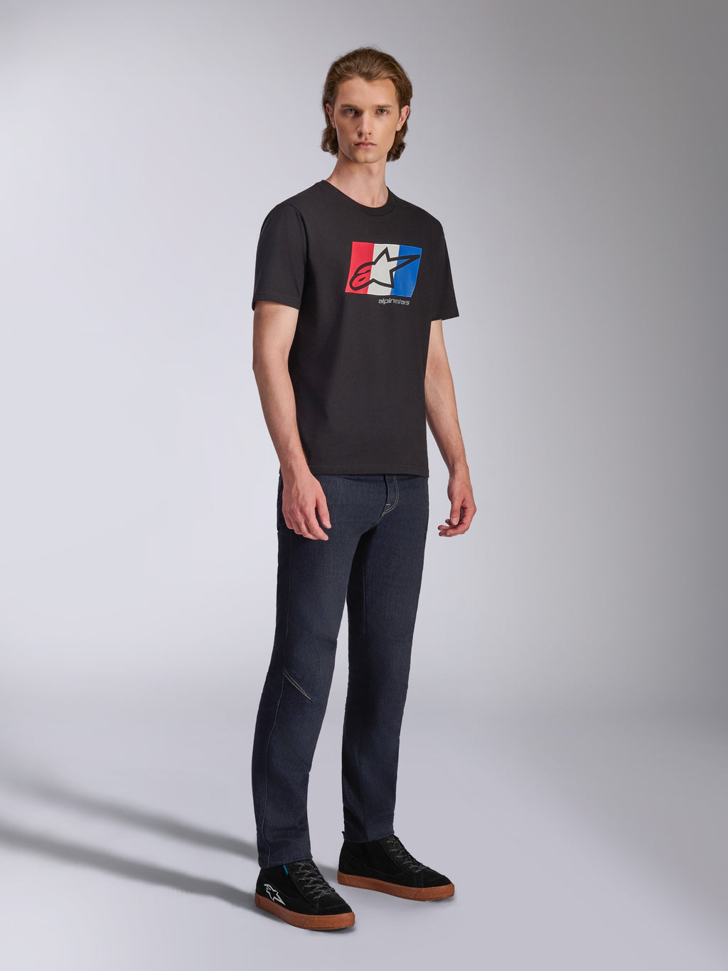Alpinestars Global CSF Tee, T-shirt met korte mouwen, zwart met rood, wit en blauw grafisch logo, casual motorsport streetwear, volledige opname van model in donkere jeans en zwarte sneakers