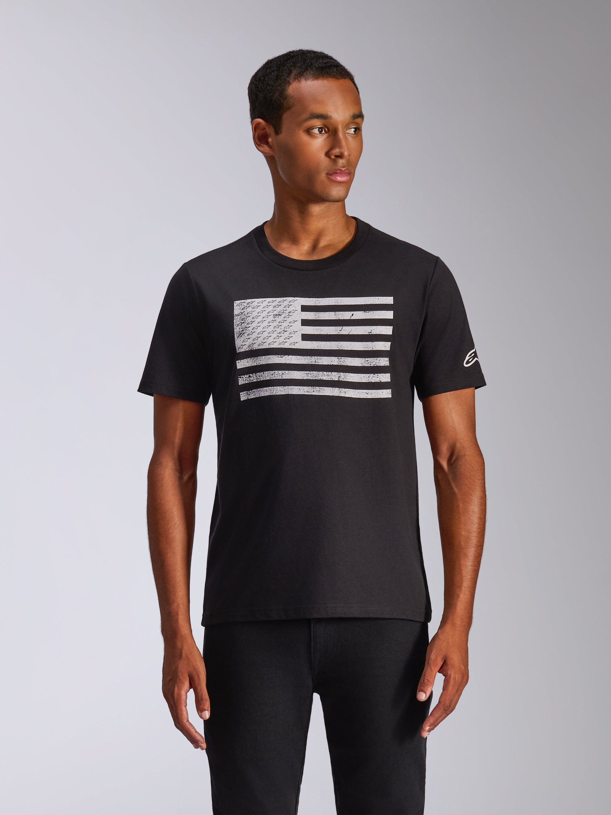Alpinestars Waving CSF T-shirt, T-shirt met korte mouwen, zwart, verweerde witte vlag-print met geïntegreerde logo's, klein wit logo op de mouw, gedragen door een model, casual motorsport streetwear