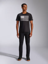 Alpinestars Waving CSF Tee, T-shirt met korte mouwen, zwart, met een verweerde witte graphic in vlagstijl op de borst, gedragen door een model met zwarte broek en zwarte hoge sneakers, casual motorsport streetwear