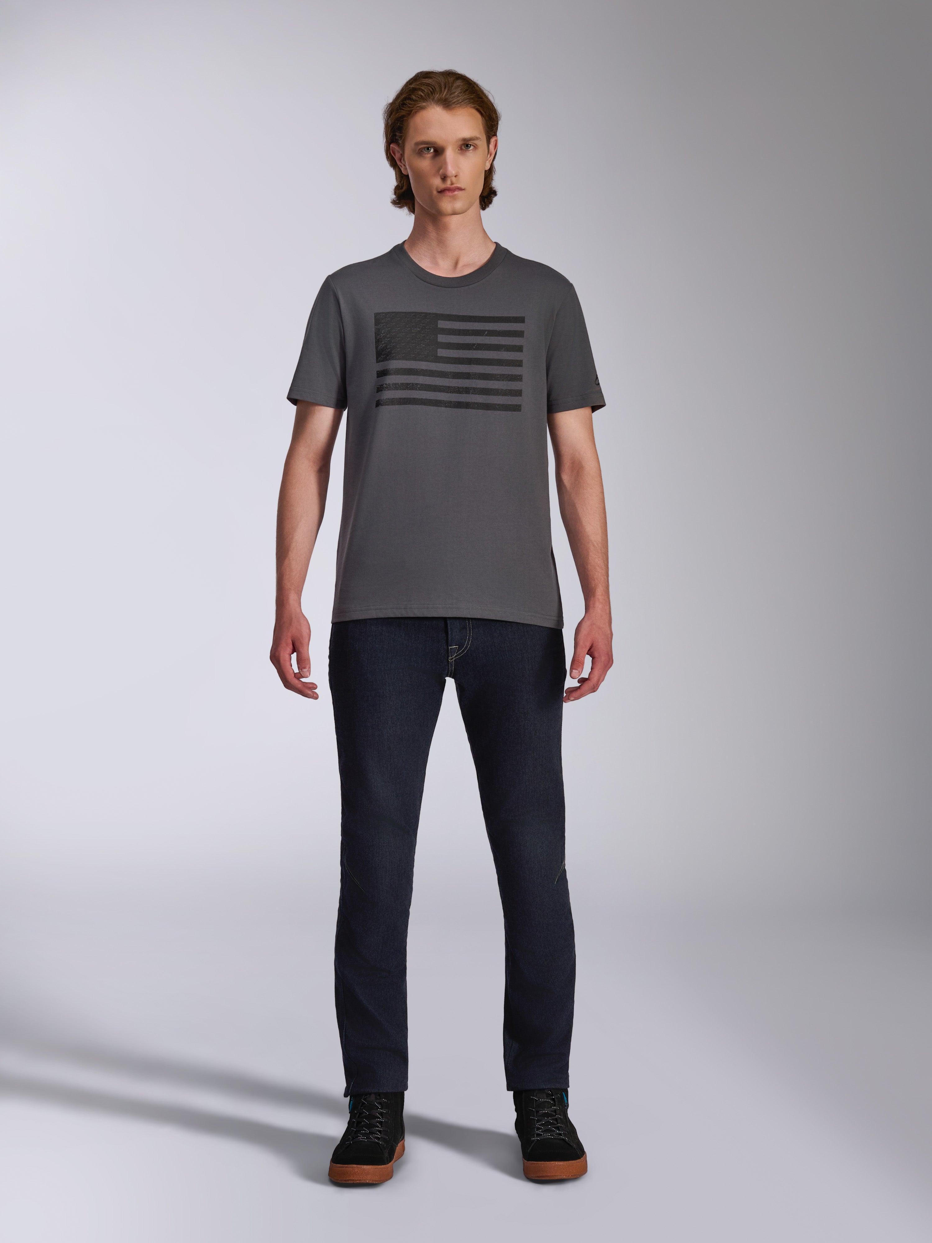 Alpinestars Waving CSF Tee, T-shirt met korte mouwen, houtskoolgrijs, zwarte Blaze 2.0 vlag-stijl logo-opdruk, casual motorsport streetwear, gedragen met donkere denim jeans