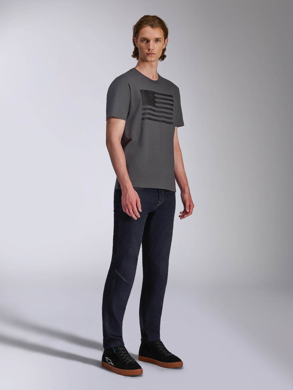 Alpinestars Waving CSF Tee, T-shirt met korte mouwen, antraciet, zwarte grafische print van een wapperende vlag, gedragen door een model met donkere jeans en sneakers, casual motorsport streetwear