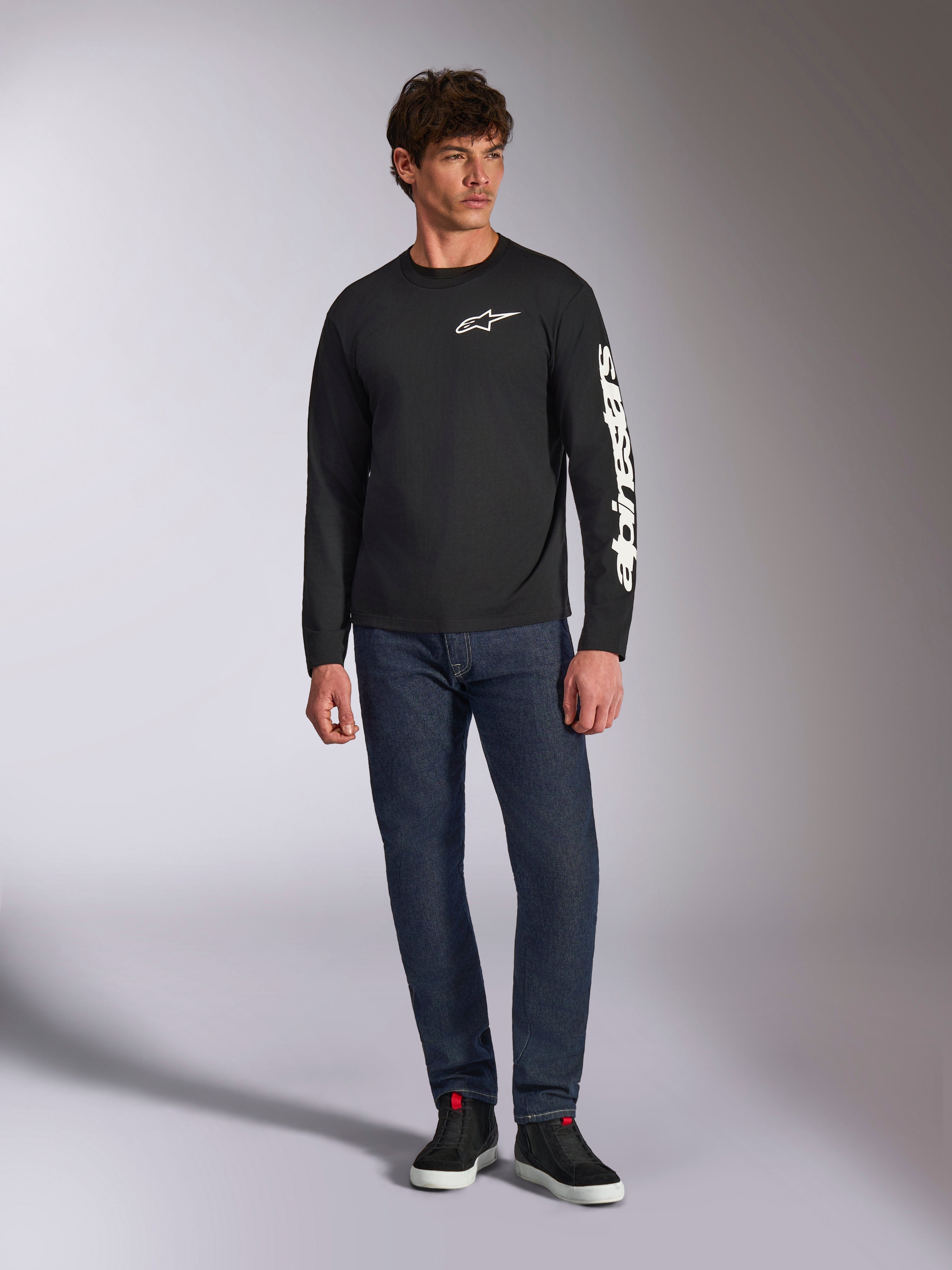 Alpinestars Trackside CSF Tee, Long Sleeve T-Shirt, Black and White, worn with dark blue jeans and black sneakers, featuring white Ride 4.0 logo on the chest and Alpinestars wordmark on the sleeve, casual motorsport-inspired streetwear