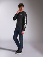 Alpinestars Trackside CSF Tee, Long Sleeve T-Shirt, Black, white vertical Alpinestars branding on sleeve and chest logo, worn by male model with dark blue jeans and sneakers, casual motorsport streetwear