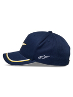 Alpinestars Ascension Snapback pet, marineblauw en goud, zijaanzicht met gebogen klep voorzien van goud en witte dubbele sutache-afwerking, geborduurd logo aan de zijkant, casual motorsport streetwear