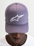 Alpinestars Ageless Snapback pet, casual sportswear pet in paars en wit, met gebogen klep, gestructureerde kroon en geborduurd 3D Astars-logo op de voorkant, gedragen door een model