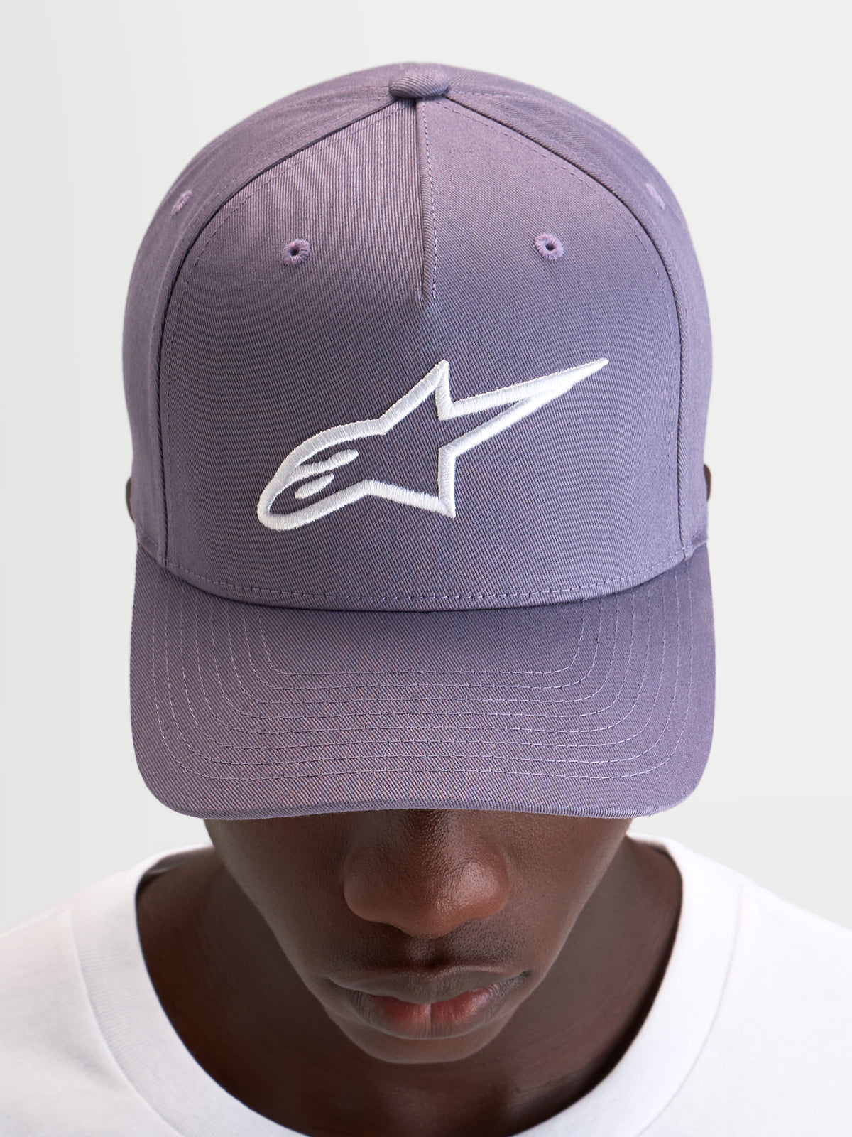 Alpinestars Ageless Snapback pet, casual sportswear pet in paars en wit, met gebogen klep, gestructureerde kroon en geborduurd 3D Astars-logo op de voorkant, gedragen door een model