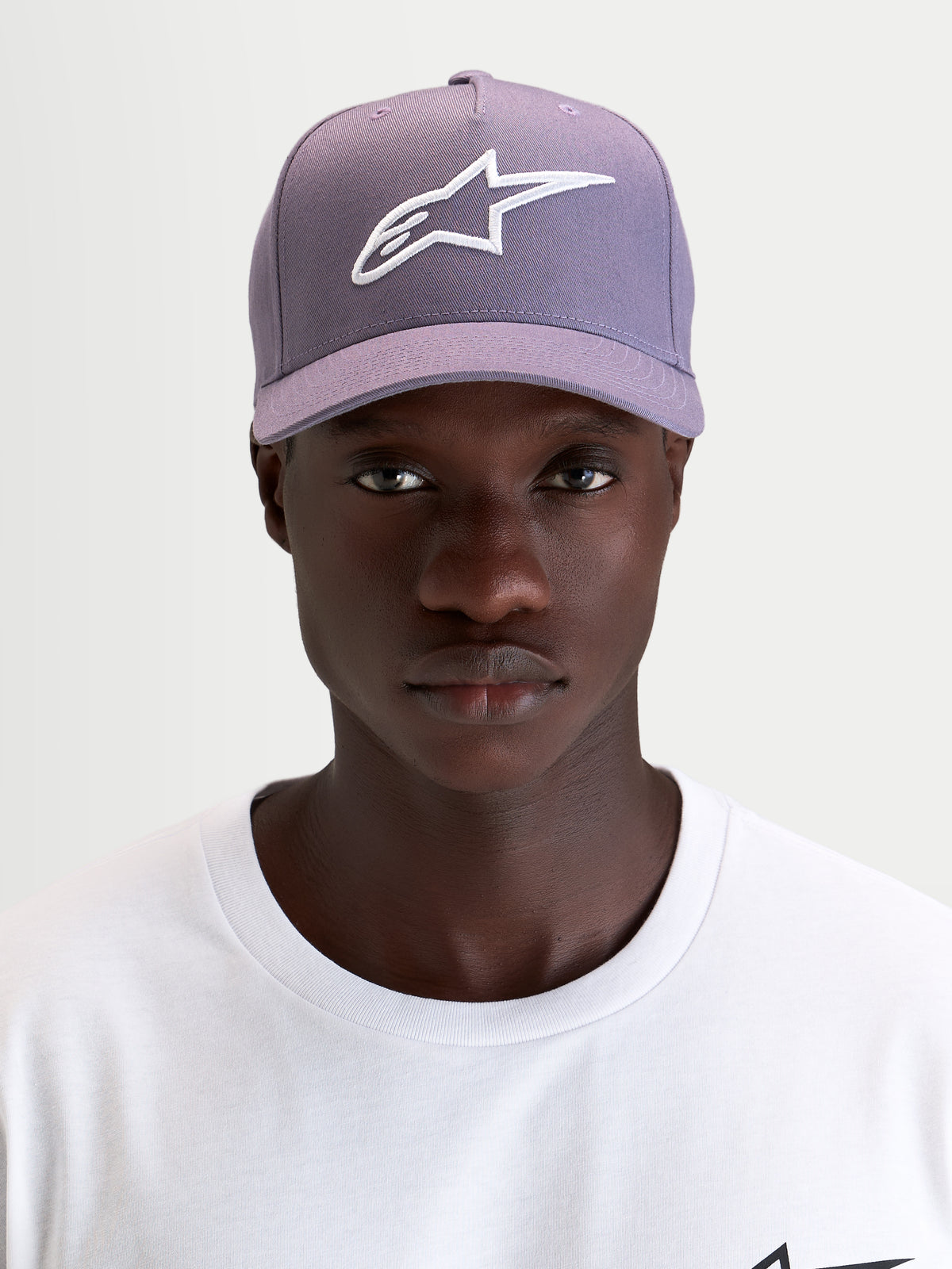 Alpinestars Ageless Snapback Pet, sportswear pet met gebogen klep, stoffen constructie in stoffig paars en wit, gedragen door een model met het geborduurde 3D Astars-logo op de voorkant