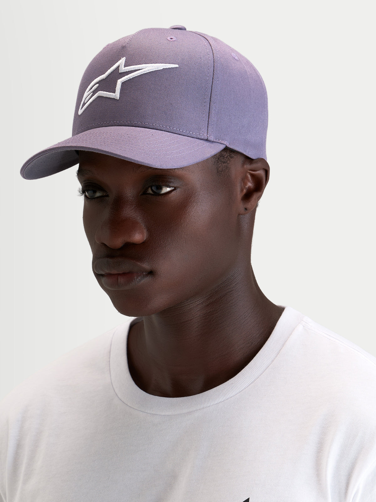 Alpinestars Ageless Snapback Pet, sportswear-pet met gebogen klep in paars en wit, gedragen door een model met de gestructureerde kroon en het geborduurde 3D Astars-logo