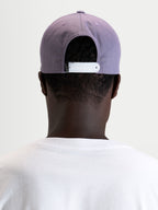 Alpinestars Ageless Snapback Pet, paarse sportswear-pet met verstelbare witte snapbacksluiting en gestructureerde kroon, gedragen vanaf de achterkant