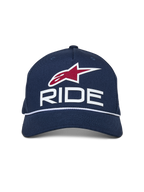 Alpinestars Ride Comp Snapback pet, donkerblauw met witte en rode accenten, voorzien van een 3D RIDE-logo, rood ster-embleem en witte gevlochten koordafwerking, gebogen klep, casual motorsport-pet