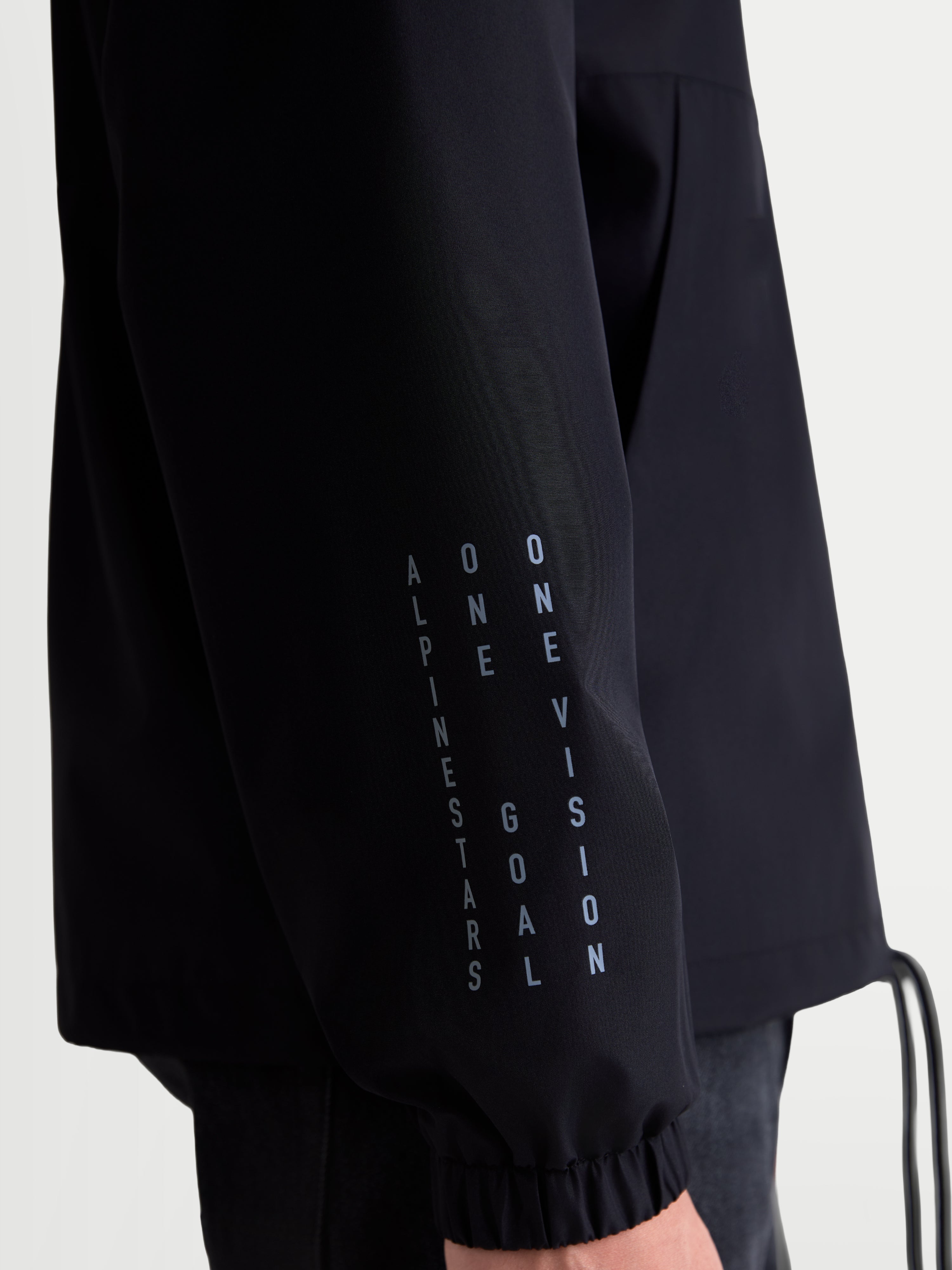Alpinestars Speeder Resolve Windbreaker Jas, zwarte lichtgewicht sportswearjas, close-up van de mouw met verticale branding en elastische manchet, winddichte 100% polyester constructie voor urban gebruik.