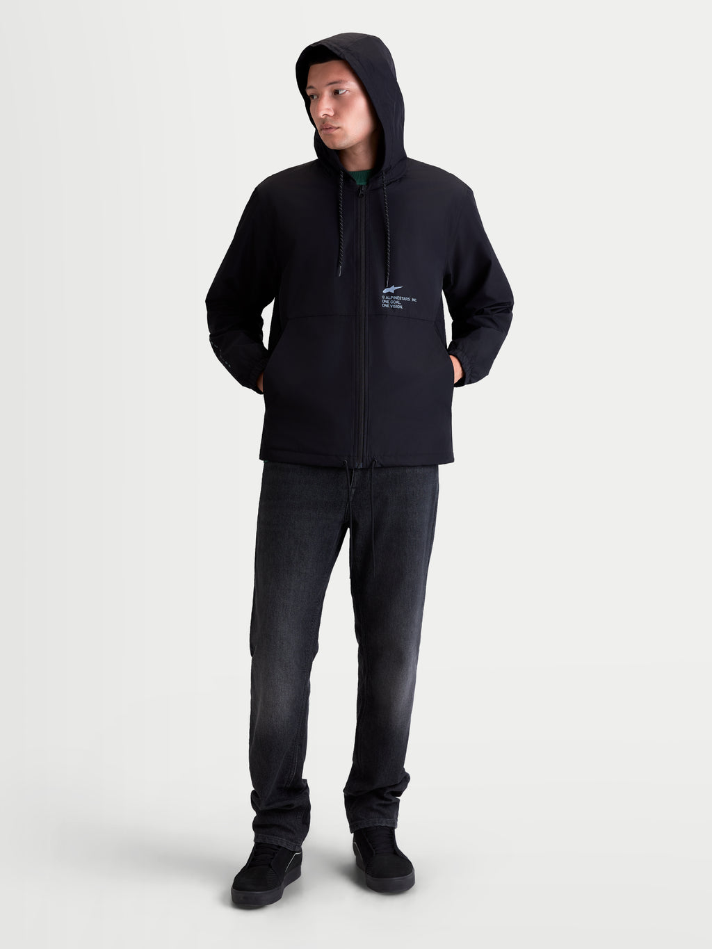 Alpinestars Speeder Resolve Windbreaker Jas, lichte heren-sportswear voor urban gebruik, zwart, 100% polyester, met een verstelbare capuchon, meshvoering en kenmerkende Alpinestars-branding op de borst. Volledig overzicht van model die de winddichte jas met capuchon draagt voor casual dagelijks gebruik.