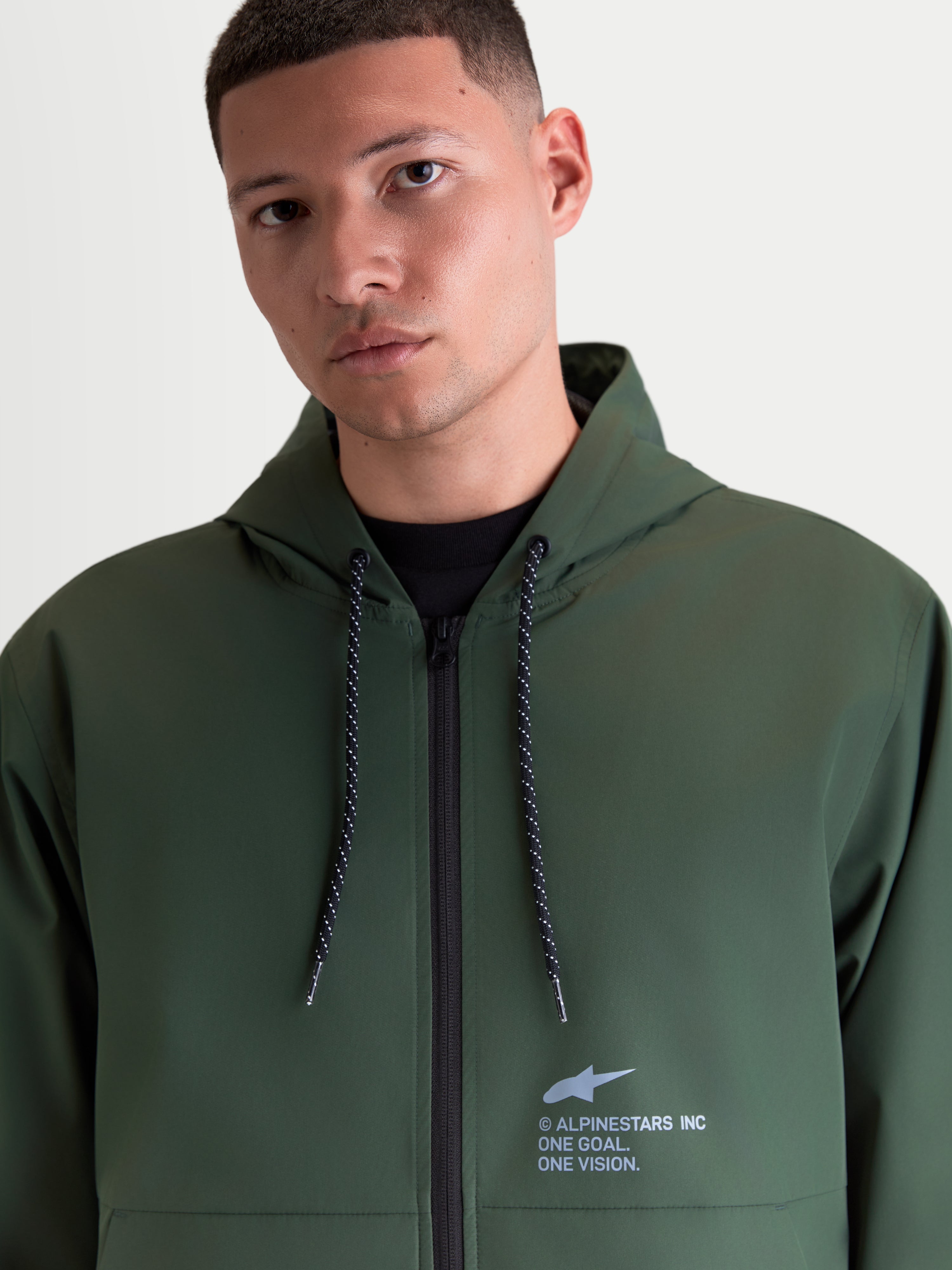 Alpinestars Speeder Resolve Windbreaker Jas, lichtgewicht herenwindbreaker in groen, voorzien van een verstelbare capuchon met gespikkelde trekkoorden en Alpinestars branding op de borst, gedragen door een model.