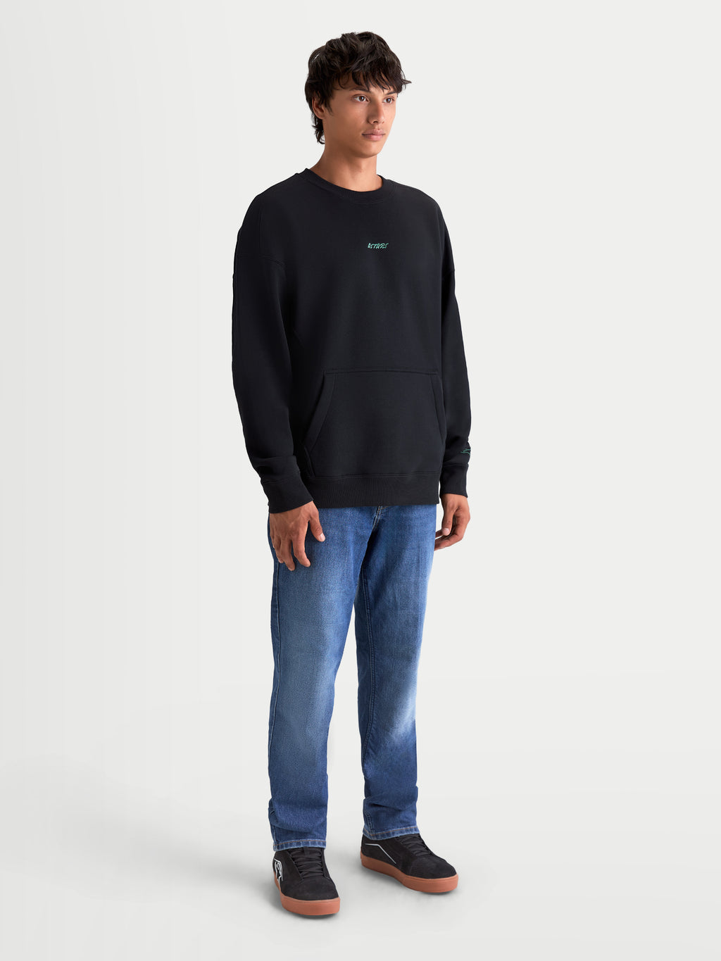 Alpinestars Guise Oversized Crew, premium sportswear pullover voor heren, relaxte oversized pasvorm, zwart met teal geborduurd logo op de borst, voorzien van kangoeroezak en geribde boorden, zachte fleece van katoen en gerecycled polyester.