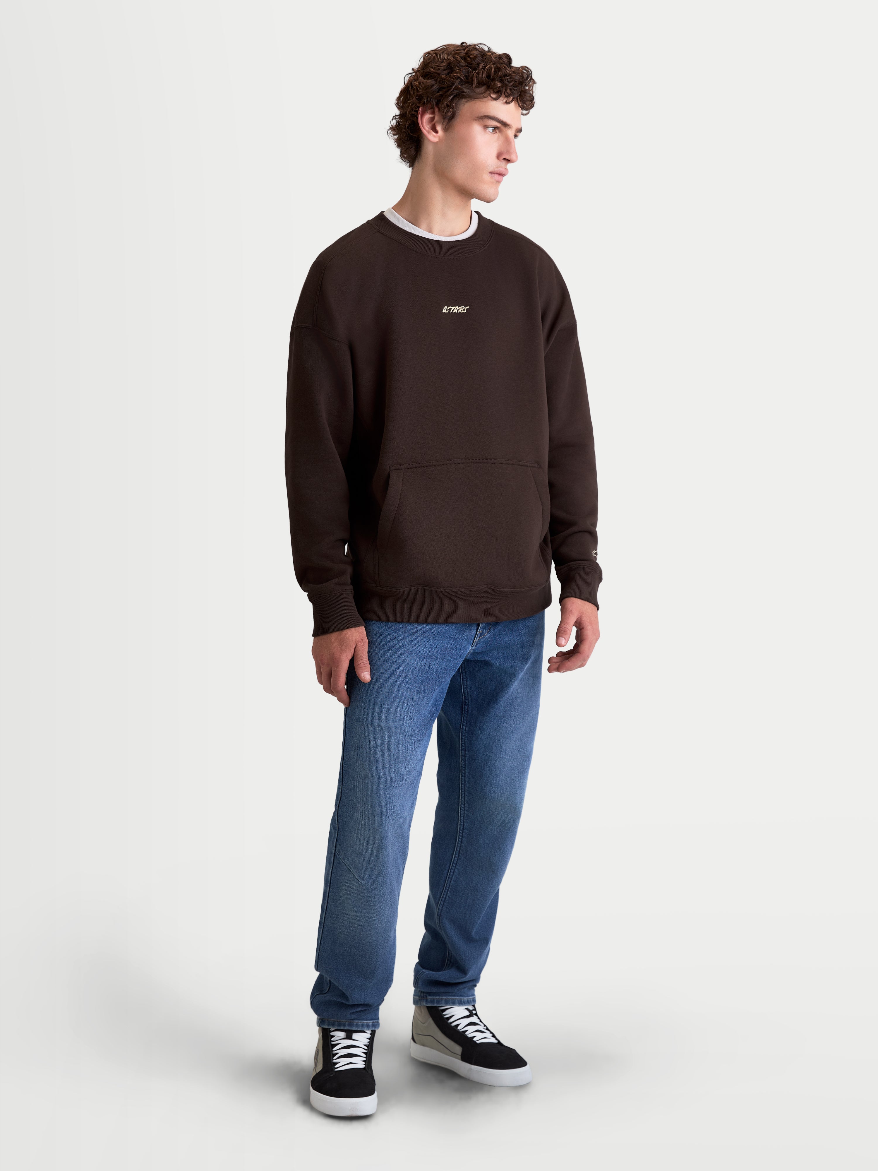 Alpinestars Guise Oversized Crew, bruine herentrui met ronde hals, oversized pasvorm met kangoeroezak en geborduurd Astars-logo, casual sportswear van katoen en gerecycled polyester, op-model weergave.