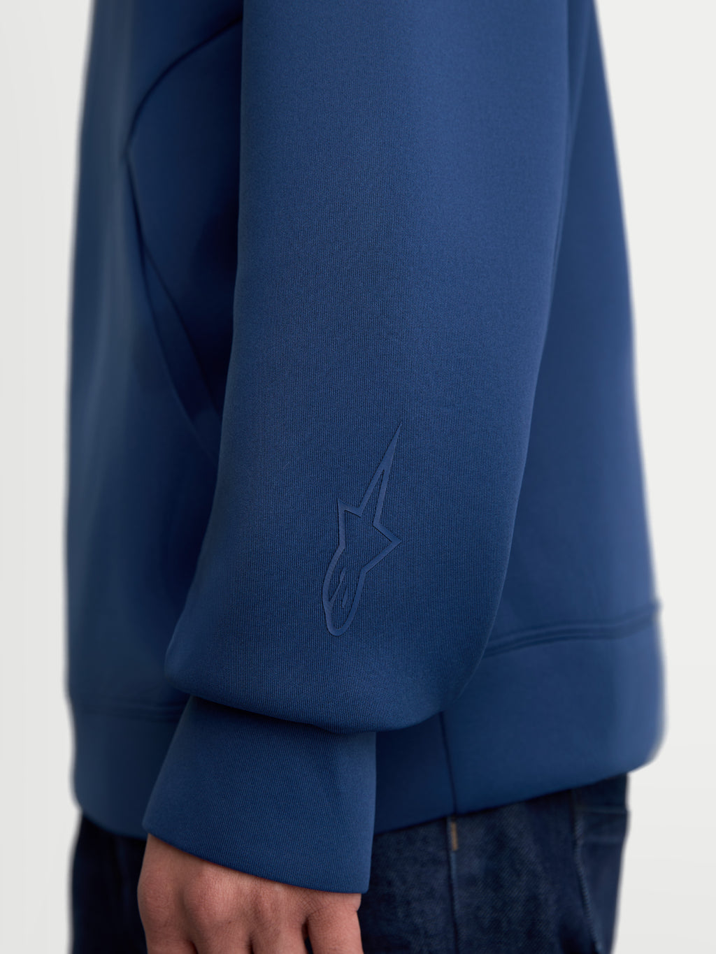 Alpinestars Datrix hoodie, premium sportswearhoodie in blauw, close-up van de mouw met een tonaal HD Alpinestars-logo, gemaakt van tri-blend dubbelzijdige fleecestof voor dagelijks comfort.