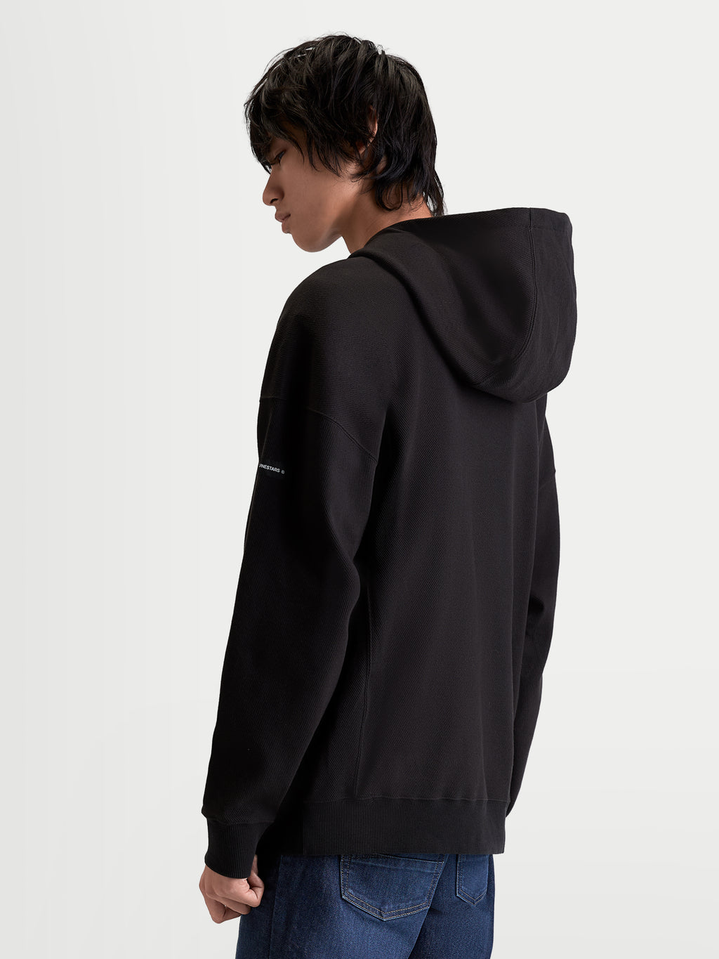 Alpinestars Camino Textured Oversized Hoodie, Sportswear Pullover for Men, Black, featuring textured knit twill fleece, high collar, and self-lined hood, back view showing relaxed silhouette and woven sleeve label.