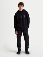 Alpinestars Shaw Oversized Hoodie, heren casual sportswear pullover, zwart, relaxte pasvorm fleece met getextureerd Alpinestars woordlogo op de borst, kangoeroezak en zelfgevoerde capuchon, vooraanzicht op model