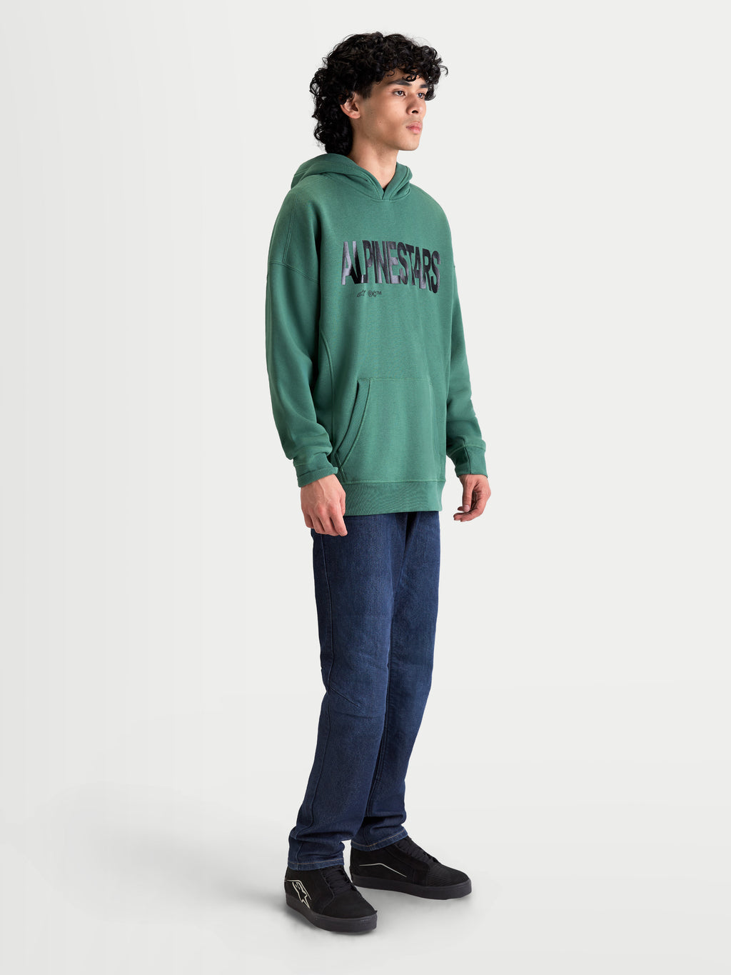 Alpinestars Shaw Oversized Hoodie, herensportswear-pullover, groen, getextureerd woordlogo, kangoeroezak, relaxte oversized pasvorm, zachte katoen en gerecycled polyester fleece, getoond op een model.