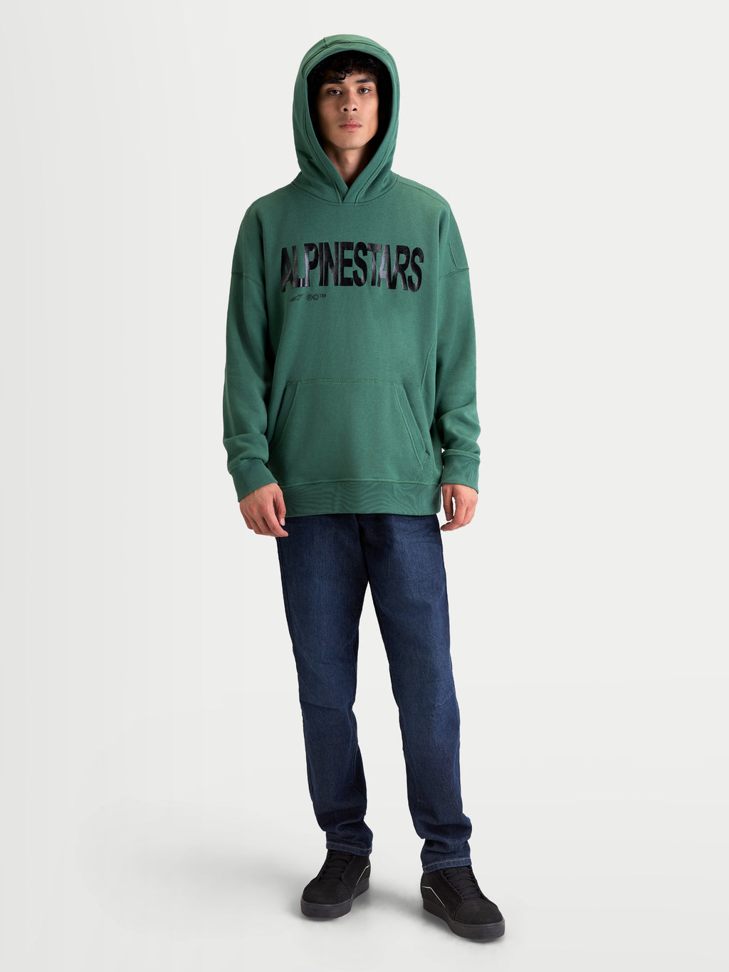 Alpinestars Shaw Oversized hoodie, relaxte sportswearpullover voor dagelijks comfort, groen met een zwart getextureerd woordlogo, vooraanzicht op model, zachte fleece van katoen en gerecycled polyester, voorzien van een kangoeroezak en ribboorden.