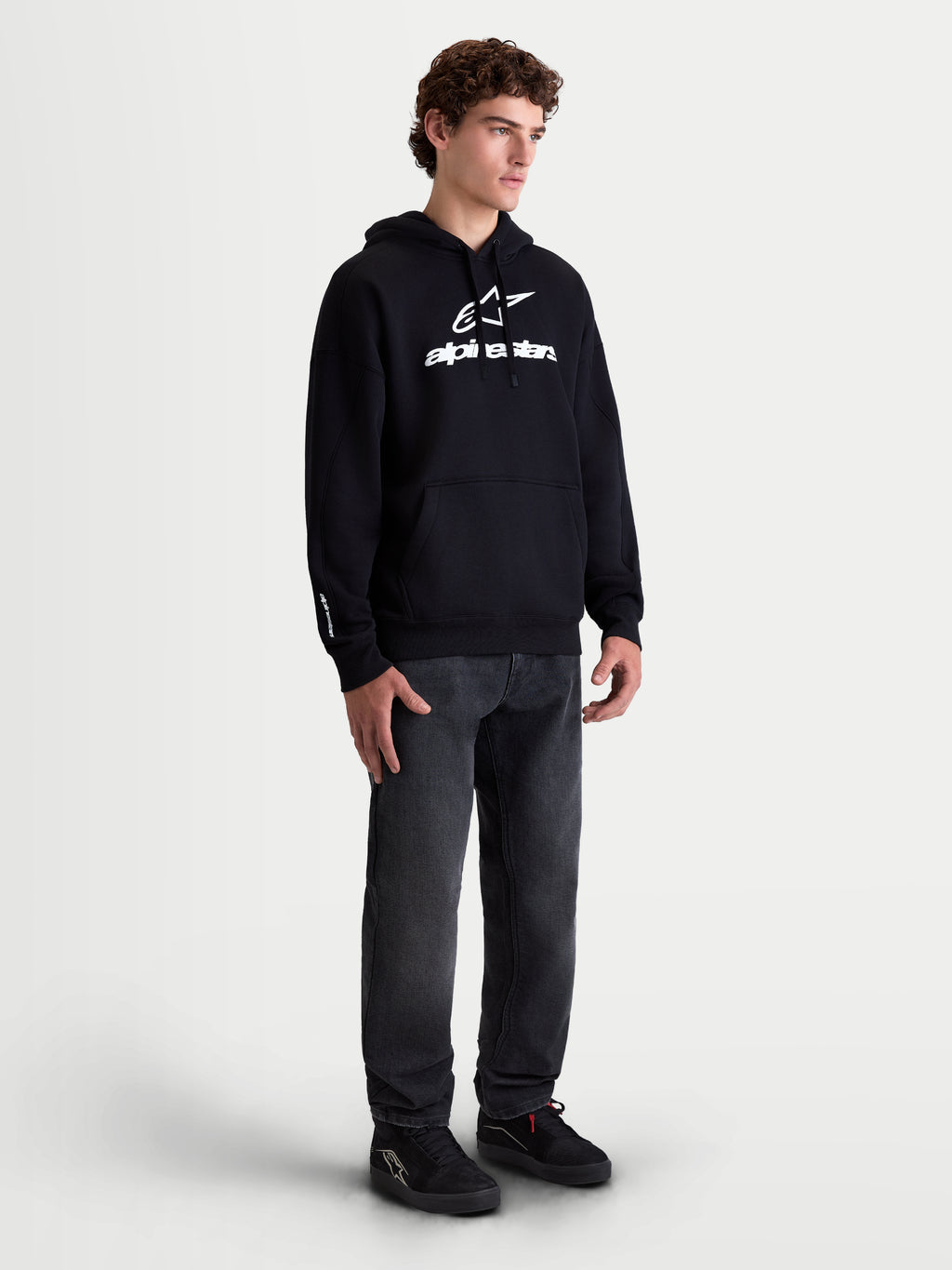 Alpinestars Prelude Oversized Hoodie, heren sportswear fleece pullover, zwart met wit puffprint-logo op de borst en mouw, relaxte oversized pasvorm en kangoeroezak, getoond op een model.