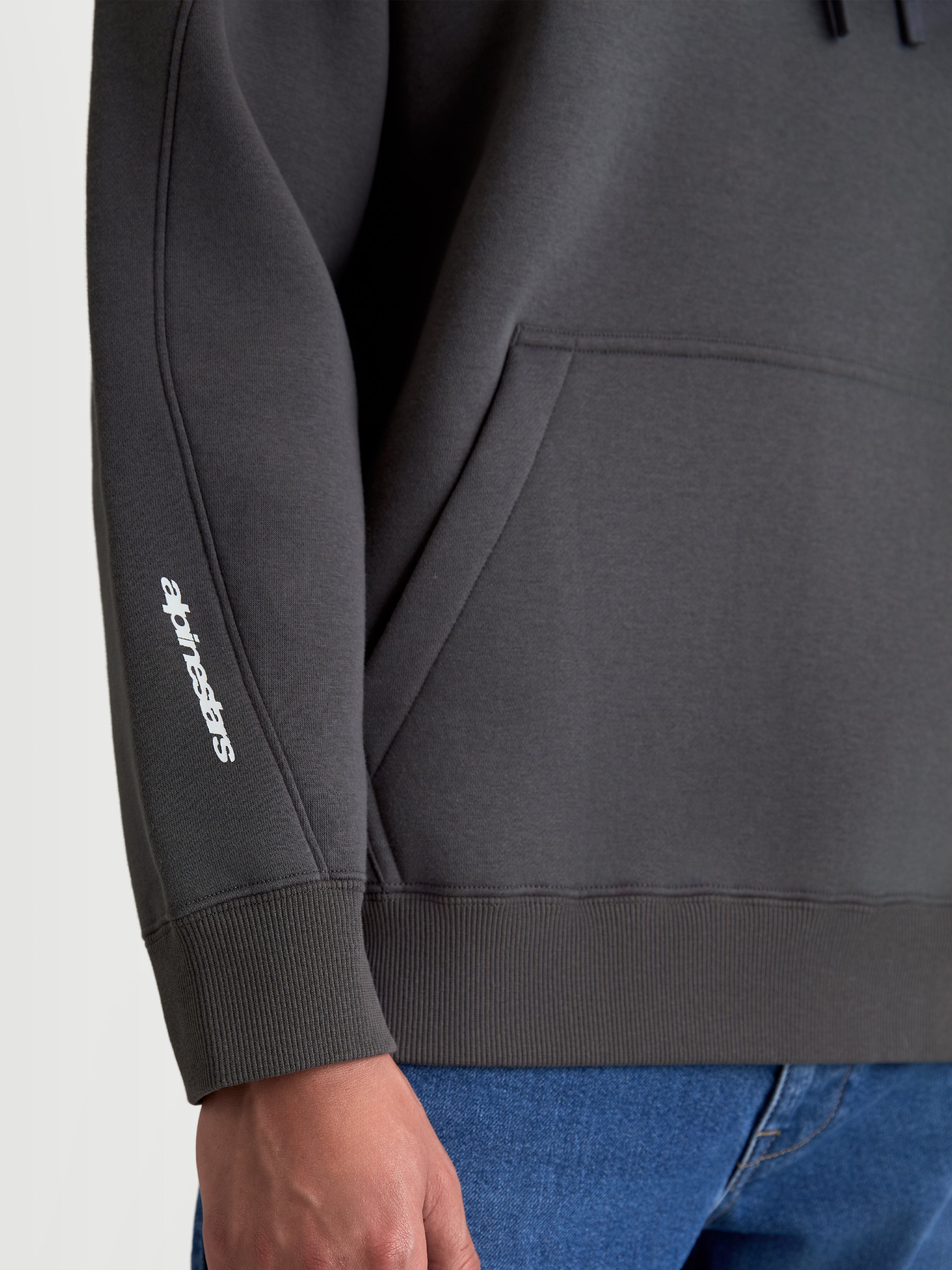 Alpinestars Prelude Oversized Hoodie, grijze sportswear fleece pullover, detailweergave van de mouwnaden, ribmanchet en wit Alpinestars-logo op de arm, relaxte pasvorm met kangoeroezak.