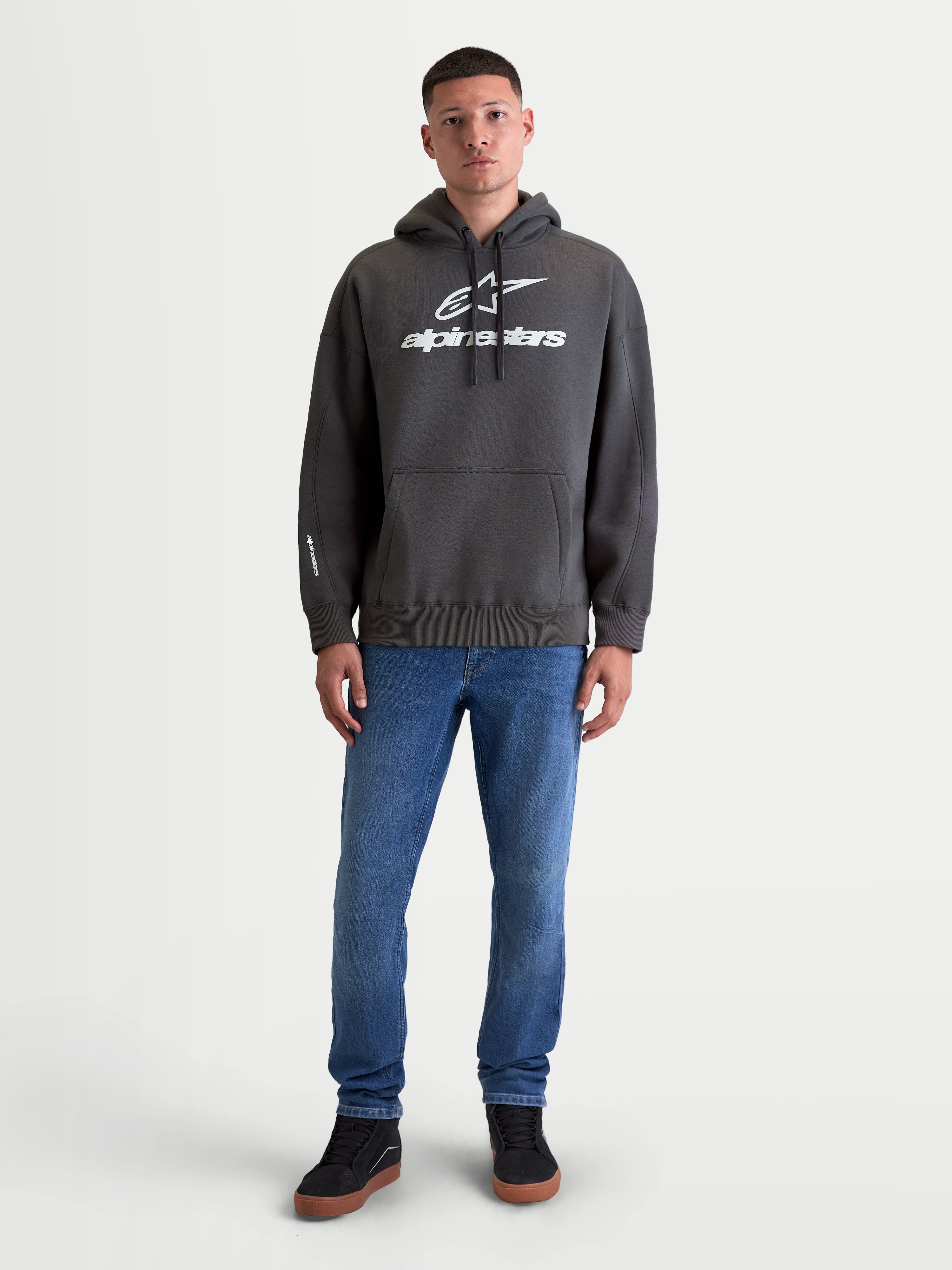 Alpinestars Prelude oversized hoodie, heren sportswear fleece pullover, antracietgrijs en wit, met een relaxte oversized pasvorm, kangoeroezak en puff-print logo's op de borst en mouw, getoond op model voor casual gebruik.