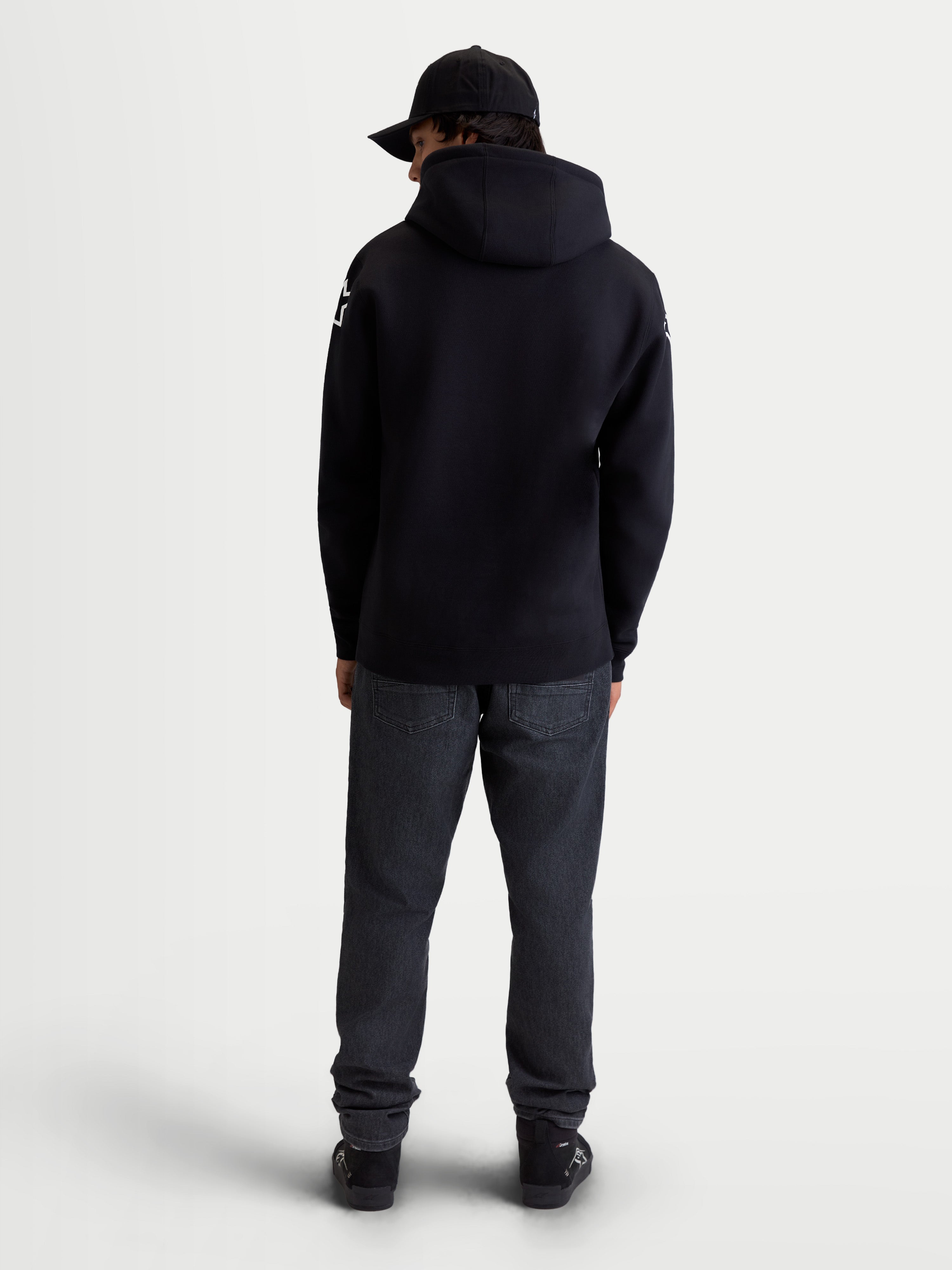 Alpinestars Velocifier hoodie, heren sportswear fleecepullover, zwart en wit, mix van katoen en gerecycled polyester, achteraanzicht op model met witte Alpinestars-logo's op de schouders en capuchon.
