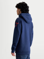 Alpinestars Velocifier Hoodie op model, heren-sportswear pullover fleece in marineblauw en rood, voorzien van een gevoerde capuchon en het iconische Astars-schouderlogo, casual off-bike motorsportkleding.