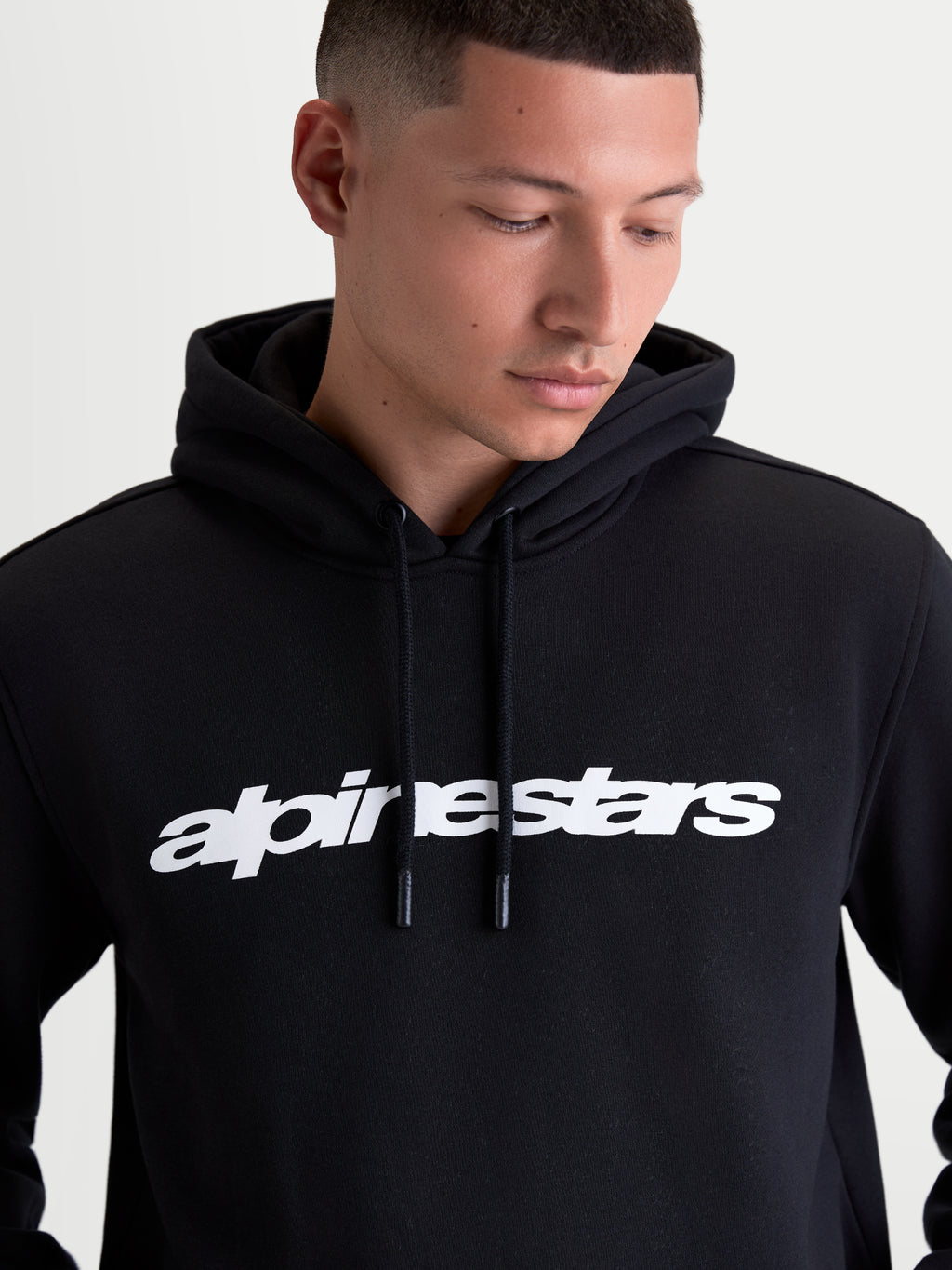 Alpinestars Race Wordmark Hoodie gedragen door een model, zwarte sportswear-hoodie met een opvallend wit woordmerklogo op de borst, gevoerde capuchon en trekkoorden met coating, gemaakt van premium katoen en gerecycled polyester fleece.