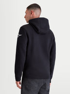 Alpinestars Race Wordmark hoodie, casual sportswear pullover fleece, achteraanzicht op model, zwart en wit, met het witte Ageless star-logo op de linkermouw, een gevoerde capuchon en geribde boorden. Gemaakt van een hoogwaardige mix van katoen en gerecycled polyester voor dagelijks comfort.