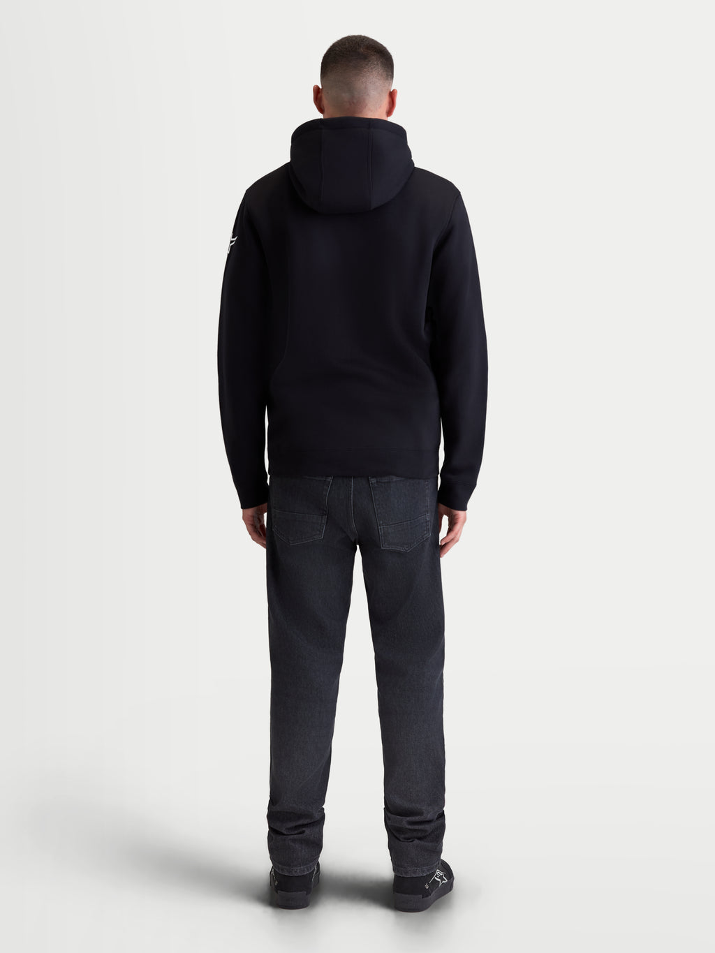 Alpinestars Race Wordmark Hoodie, heren-sportswear fleece hoodie, zwart en wit, achteraanzicht van model die de zwarte hoodie draagt, voorzien van een gevoerde capuchon en comfortabele katoenmix voor een motorsport-geïnspireerde lifestyle.