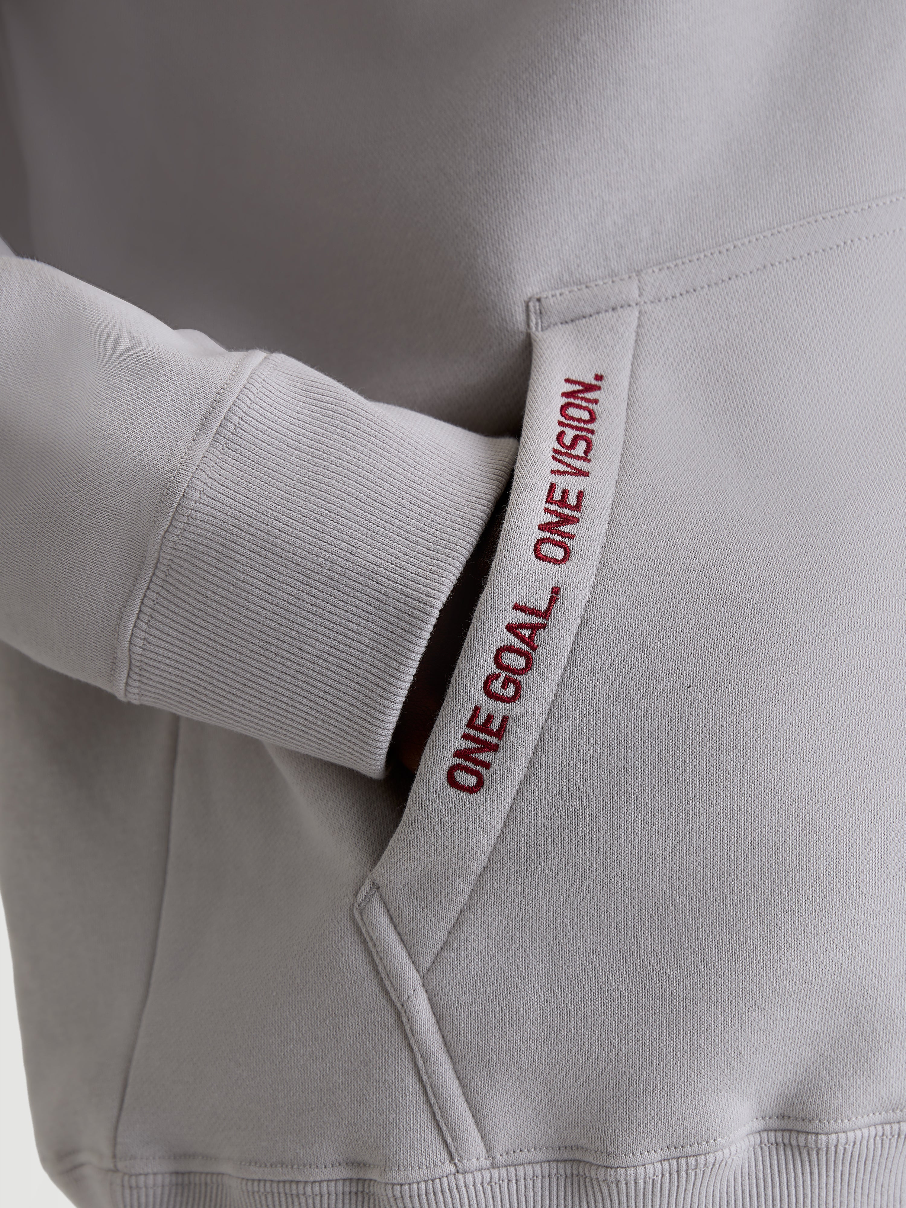 Alpinestars Pioneer Oversized Hoodie, Casual Sportswear Fleece in Cement Gray, Close-up of Kangaroo Pocket with Red 'ONE GOAL. ONE VISION.' Embroidery and Ribbed Cuffs