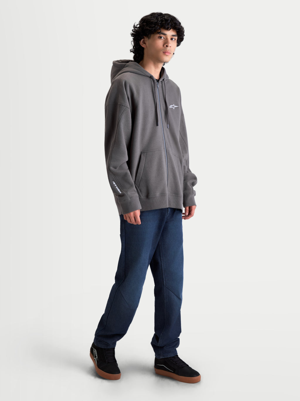 Alpinestars Entity oversized hoodie, sportswear fleece hoodie met ritssluiting, grijs, voorzien van een oversized pasvorm, Vislon-rits aan de voorzijde, kangoeroezakken en wit geborduurd Alpinestars-logo op de borst en mouw. Casual motorsportgeïnspireerde lifestyle kleding gedragen door een model.