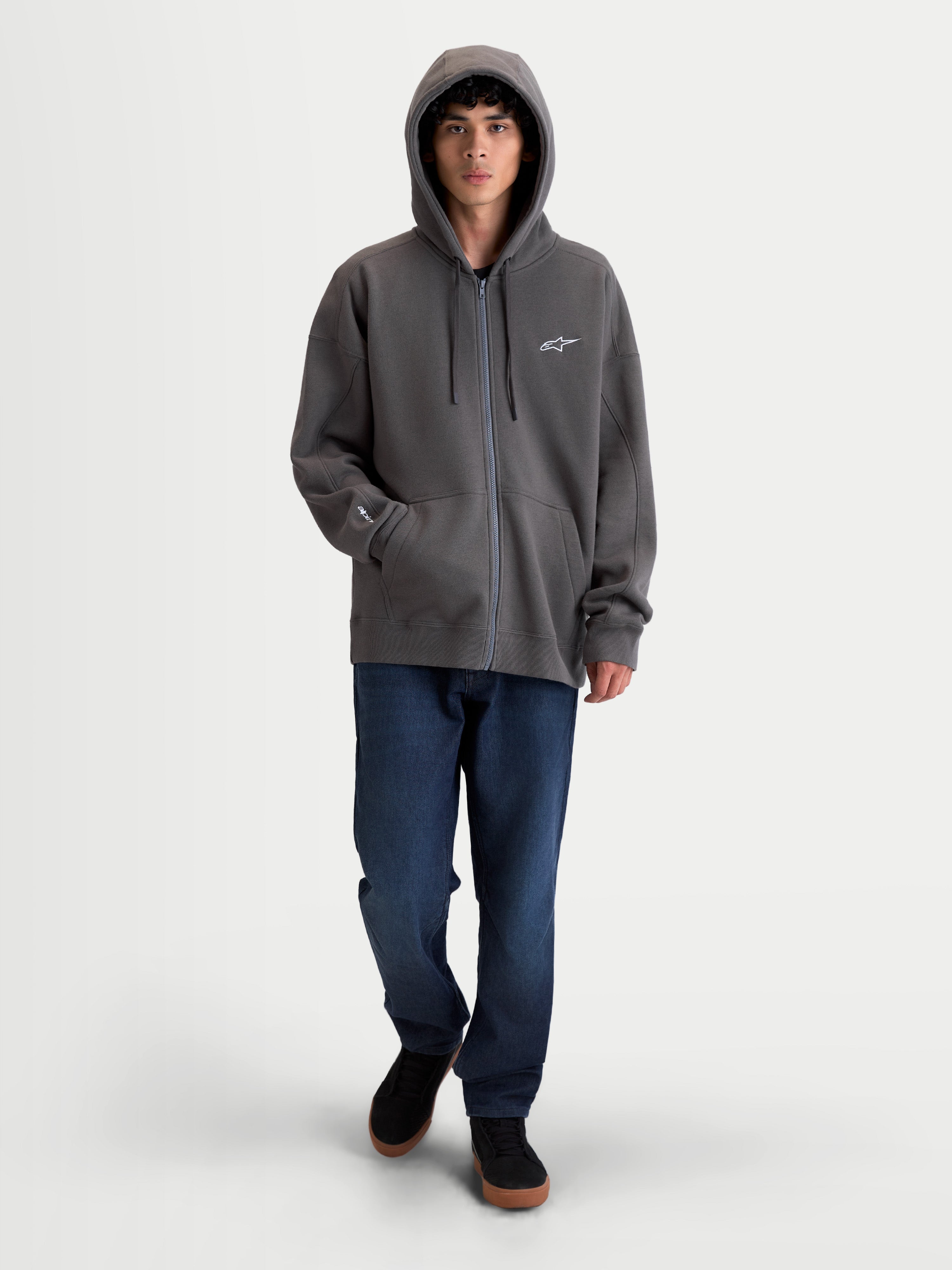 Alpinestars Entity Oversized Hoodie, premium motorsport fleece hoodie met rits, grijs, voorzien van een Vislon-ritssluiting, gevoerde capuchon met trekkoorden en kangoeroezak. On-model weergave van het relaxte silhouet met geborduurd Astars-logo op de borst en mouw.