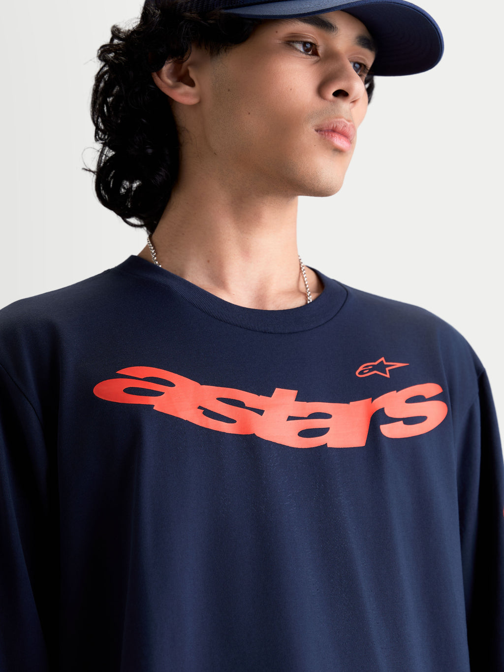 Alpinestars Velocifier CSF T-shirt met lange mouwen, motorsport-geïnspireerde casual sportswear op model, blauw met een gebogen oranje Astars-graphic op de borst, zachte katoenmix.