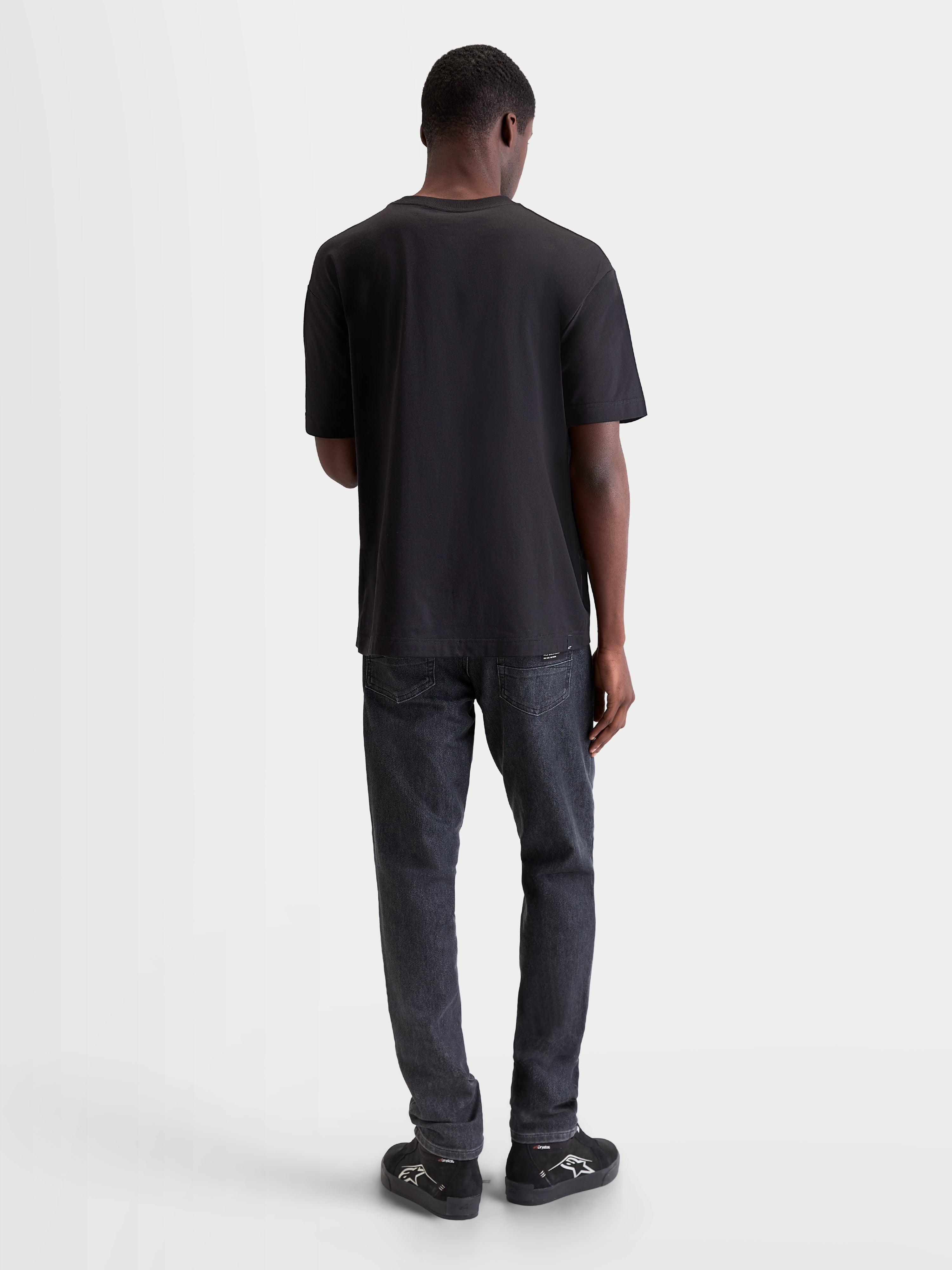 Alpinestars Infinity Oversized CSF t-shirt, zwart sportswear t-shirt met korte mouwen, achteraanzicht op model, relaxed fit voor dagelijks comfort en stijl naast de motor.
