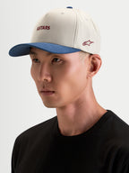 Alpinestars County Canvas pet, sportswear pet in zand en blauw, gedragen door een model, met een gebogen klep en geborduurde Astars-logo's