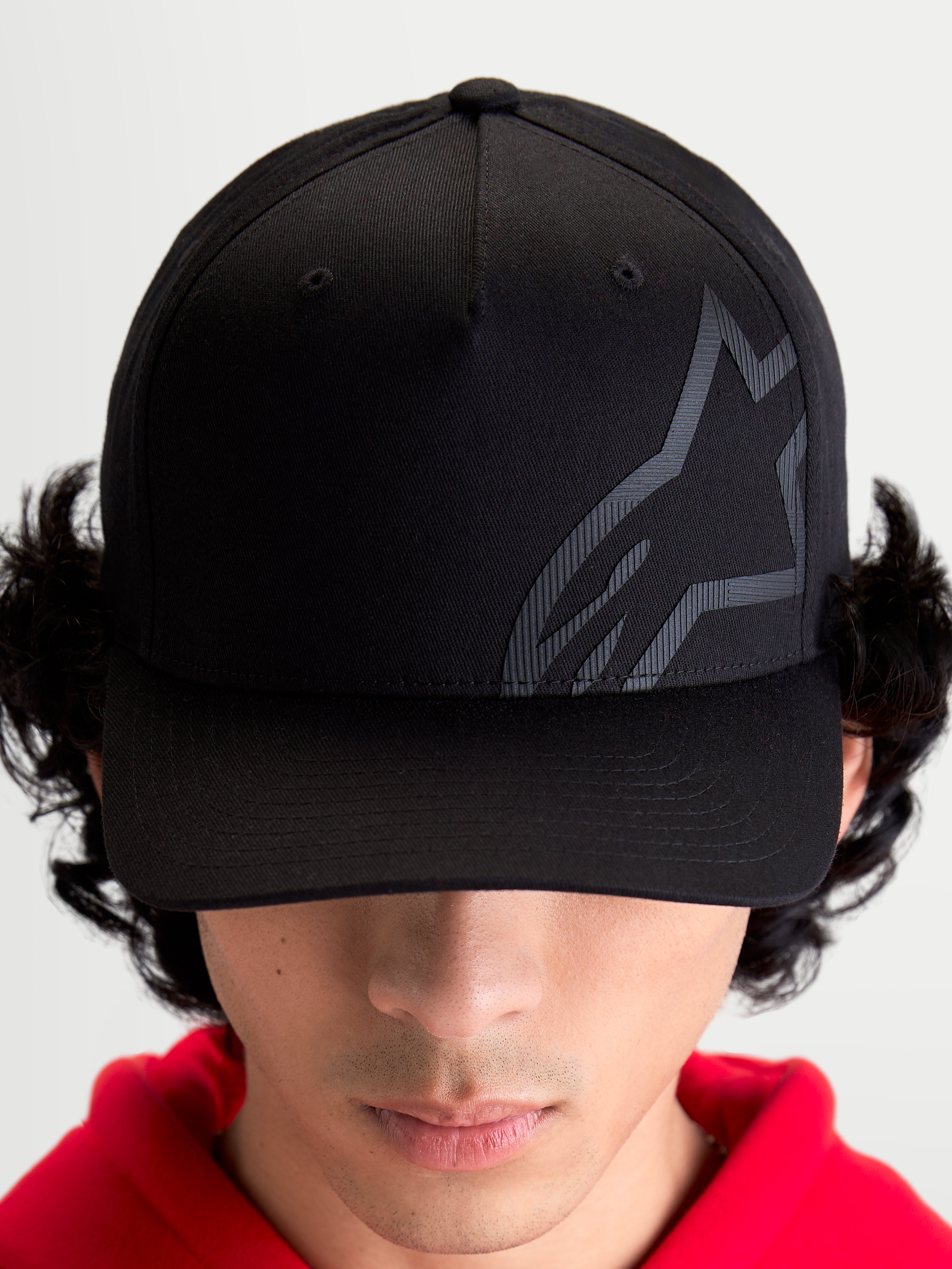 Alpinestars Maze pet, motorsport-geïnspireerde sportswear baseballpet, unisex, zwart, keperstof met gestructureerde kroon, gebogen klep en getextureerd tonaal Astars Corp Shift-logo, vooraanzicht op model.