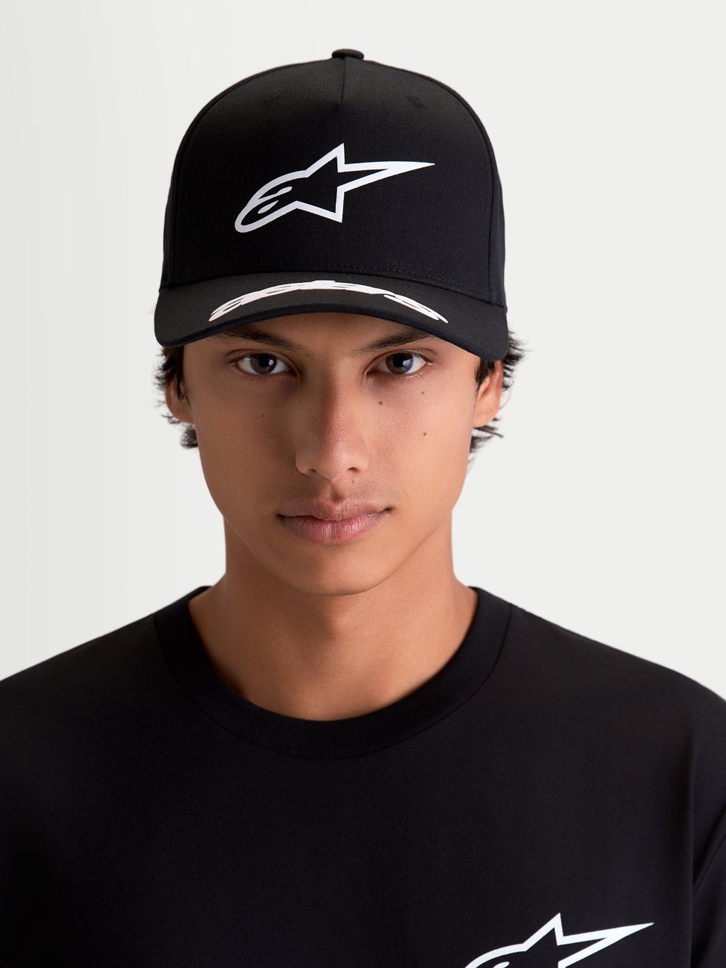 Alpinestars Arclight pet, motorsport-sportswearpet, zwart en wit, vooraanzicht op model, wit puff-print Astars-logo op gestructureerde kroon, gebogen klep met logodetails, premium keperstof