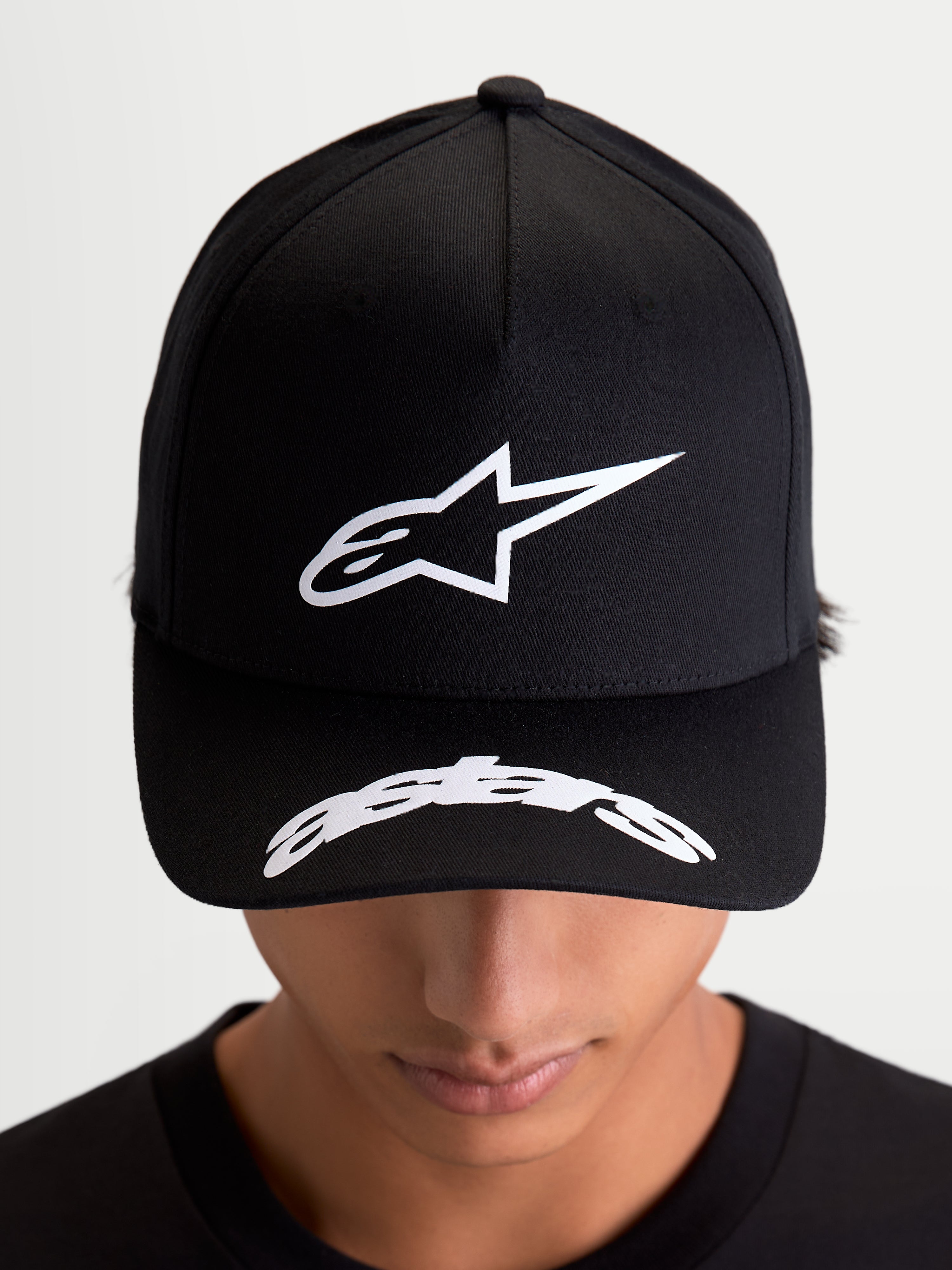 Alpinestars Arclight pet, zwarte motorsport-baseballcap, on-model vooraanzicht met wit puffprint Astars-logo op de gestructureerde kroon en gebogen woordlogo op de klep, casual sportswear van keperstof.