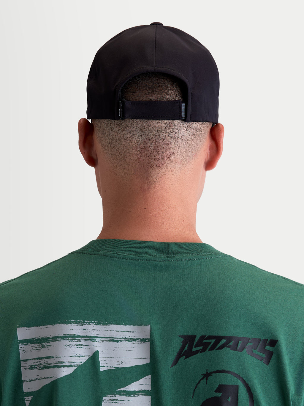 Alpinestars Algo Perf Ajustable pet, zwarte motorsport-geïnspireerde sportswear pet, achteraanzicht op model met verstelbare snapback-sluiting, technische stofconstructie, unisex.