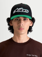 Alpinestars Retro Snapback pet, sportswear lifestyle-pet, zwart en groen, voorzien van een gebogen klep, gestructureerde kroon en geborduurd Astars-logo met groen contraststiksel op de voorzijde, getoond op model in vooraanzicht.