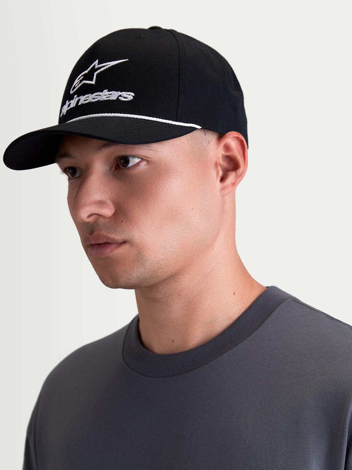 Alpinestars Combo Logo Snapback pet, zwart-witte sportswear lifestyle cap met gebogen klep, gestructureerde kroon, wit geborduurd Alpinestars combo-logo en touwdetail, getoond op een model in profielaanzicht.