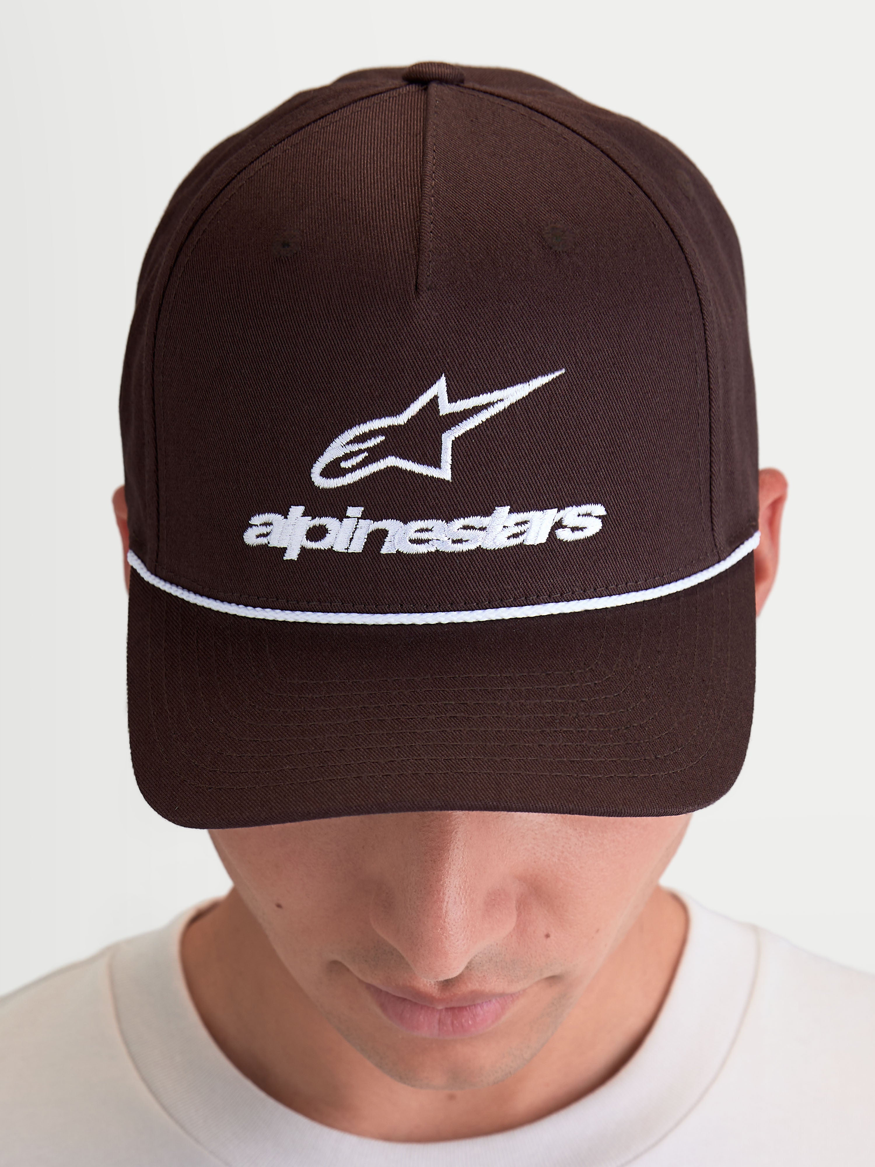 Alpinestars Combo Logo Snapback pet, casual sportswearpet, bruin met wit borduursel, voorzien van Astars-logo en woordmerk op de voorkant, gebogen klep en gestructureerde kroon, hoogwaardige katoenen keperstofconstructie, getoond op model.